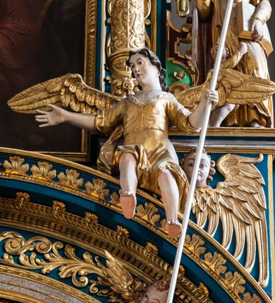 Zdjęcie nr 39: Ołtarz architektoniczny, trójosiowy, dwukondygnacyjny ze zwieńczeniem. Mensa prostopadłościenna, kamienna z drewnianym antepedium w formie leżącego prostokąta z postacią św. Augustyna ujętego wicią suchego akantu z przeplecioną, karbowaną wstążką i bukietami kwiatów. Przedstawienie otoczone profilowaną, ażurową ramą wypełnioną podobną wicią z akantu i kwiatów. Na mensie prostopadłościenne tabernakulum w formie kapliczki. Ściana frontowa z drzwiczkami w kształcie stojącego prostokąta dekorowanego krzyżem łacińskim ujętym wicią roślinną, zwieńczona trójkątnym przyczółkiem. Ścianka ujęta lizenami wypełnionymi wicią akantową podtrzymującymi pełne belkowanie obiegające bryłę, z mocno wysuniętym gzymsem wyłamanym w narożach. Całość zwieńczona czterospadowym dachem dekorowanym łuską. Na dachu baranek Boży leżący na księdze z siedmioma pieczęciami, przytrzymujący chorągiew, ukazany na tle chrystogramu otoczonego glorią promienistą. 
Nastawa na dwudzielnym cokole z półkolistymi bramkami ze zwieńczeniem utworzonym z ornamentu okuciowego ujmującego owalne pola. Osie pierwszej kondygnacji wydzielone kolumnami stojącymi na konsolach dekorowanych z frontu uskrzydlonymi główkami anielskimi powyżej liści akantu, na krawędziach cekinami, a po bokach wicią. Kolumny zostały przedzielone opaską w jednej trzeciej wysokości, dekorowane na całej wysokości wicią roślinną, główkami anielskimi w dolnej partii i imitacją kameryzacji na opaskach oraz w dwóch trzecich wysokości. Kolumny są ustawione na tle pilastrów dekorowanych wicią roślinną i zawieszonymi na niej chustkami. W polu centralnym kondygnacji jest nisza w kształcie stojącego prostokąta zamkniętego łukiem pełnym z postacią ukrzyżowanego Chrystusa na tle widoku Jerozolimy. W osiach bocznych mniejsze, ujęte pilastrami nisze o podobnym kształcie, których konchy wypełnione są muszlą, zwieńczone trójkątnym przyczółkiem przerwanym na cokół. W nich, na dekorowanych wicią i rozetami konsolach ustawiono figury: po lewej stronie św. Piotra, a po prawej św. Pawła. Kondygnacje ujmują ażurowe uszaki utworzone z ornamentu okuciowego, ulistnionych wolut i przewieszonej chustki. Kolumny podtrzymują pełne belkowanie wyniesione w łuk nad polem centralnym. Podłucze dekorowane rozetami, fryz głowami anielskimi i wicią, gzyms m.in. kostkowaniem i liśćmi akantu. Całość spięta kluczem z kartuszem z herbem kanoników regularnych od pokuty (marków). Na wyniesieniu belkowania posadowiono postaci aniołów trzymających narzędzia męki: anioł po lewej włócznię, a anioł po prawej gąbkę. Górna kondygnacja oparta została na schemacie aediculi – prostokątne pole ujęto kolumnami podtrzymującymi pełne belkowanie i trójkątny przyczółek przerwany na środku na cokół, na którym ustawiono rzeźbę  pelikana karmiącego młode własną krwią. Na krawędziach przyczółka dwie leżące postaci. Kondygnacja flankowana postaciami czterech ewangelistów ustawionymi na cokołach. Po lewej stronie św. Marek i św. Jan, po prawej św. Mateusz i św. Łukasz. Struktura polichromowana na kolor ciemnoniebieski; kolumny, profile, detale i ornamenty złocone i srebrzone.
