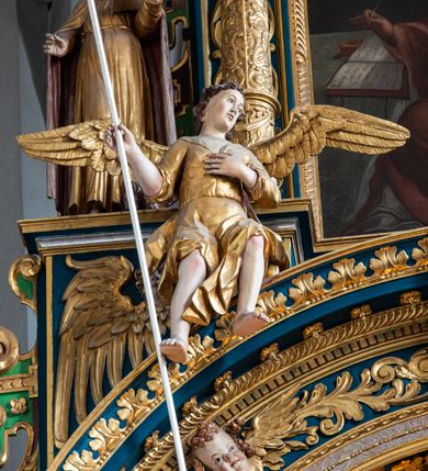 Zdjęcie nr 40: Ołtarz architektoniczny, trójosiowy, dwukondygnacyjny ze zwieńczeniem. Mensa prostopadłościenna, kamienna z drewnianym antepedium w formie leżącego prostokąta z postacią św. Augustyna ujętego wicią suchego akantu z przeplecioną, karbowaną wstążką i bukietami kwiatów. Przedstawienie otoczone profilowaną, ażurową ramą wypełnioną podobną wicią z akantu i kwiatów. Na mensie prostopadłościenne tabernakulum w formie kapliczki. Ściana frontowa z drzwiczkami w kształcie stojącego prostokąta dekorowanego krzyżem łacińskim ujętym wicią roślinną, zwieńczona trójkątnym przyczółkiem. Ścianka ujęta lizenami wypełnionymi wicią akantową podtrzymującymi pełne belkowanie obiegające bryłę, z mocno wysuniętym gzymsem wyłamanym w narożach. Całość zwieńczona czterospadowym dachem dekorowanym łuską. Na dachu baranek Boży leżący na księdze z siedmioma pieczęciami, przytrzymujący chorągiew, ukazany na tle chrystogramu otoczonego glorią promienistą. 
Nastawa na dwudzielnym cokole z półkolistymi bramkami ze zwieńczeniem utworzonym z ornamentu okuciowego ujmującego owalne pola. Osie pierwszej kondygnacji wydzielone kolumnami stojącymi na konsolach dekorowanych z frontu uskrzydlonymi główkami anielskimi powyżej liści akantu, na krawędziach cekinami, a po bokach wicią. Kolumny zostały przedzielone opaską w jednej trzeciej wysokości, dekorowane na całej wysokości wicią roślinną, główkami anielskimi w dolnej partii i imitacją kameryzacji na opaskach oraz w dwóch trzecich wysokości. Kolumny są ustawione na tle pilastrów dekorowanych wicią roślinną i zawieszonymi na niej chustkami. W polu centralnym kondygnacji jest nisza w kształcie stojącego prostokąta zamkniętego łukiem pełnym z postacią ukrzyżowanego Chrystusa na tle widoku Jerozolimy. W osiach bocznych mniejsze, ujęte pilastrami nisze o podobnym kształcie, których konchy wypełnione są muszlą, zwieńczone trójkątnym przyczółkiem przerwanym na cokół. W nich, na dekorowanych wicią i rozetami konsolach ustawiono figury: po lewej stronie św. Piotra, a po prawej św. Pawła. Kondygnacje ujmują ażurowe uszaki utworzone z ornamentu okuciowego, ulistnionych wolut i przewieszonej chustki. Kolumny podtrzymują pełne belkowanie wyniesione w łuk nad polem centralnym. Podłucze dekorowane rozetami, fryz głowami anielskimi i wicią, gzyms m.in. kostkowaniem i liśćmi akantu. Całość spięta kluczem z kartuszem z herbem kanoników regularnych od pokuty (marków). Na wyniesieniu belkowania posadowiono postaci aniołów trzymających narzędzia męki: anioł po lewej włócznię, a anioł po prawej gąbkę. Górna kondygnacja oparta została na schemacie aediculi – prostokątne pole ujęto kolumnami podtrzymującymi pełne belkowanie i trójkątny przyczółek przerwany na środku na cokół, na którym ustawiono rzeźbę  pelikana karmiącego młode własną krwią. Na krawędziach przyczółka dwie leżące postaci. Kondygnacja flankowana postaciami czterech ewangelistów ustawionymi na cokołach. Po lewej stronie św. Marek i św. Jan, po prawej św. Mateusz i św. Łukasz. Struktura polichromowana na kolor ciemnoniebieski; kolumny, profile, detale i ornamenty złocone i srebrzone.
