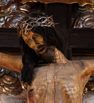 Zdjęcie nr 12: Ołtarz architektoniczny, trójosiowy, dwukondygnacyjny ze zwieńczeniem. Mensa prostopadłościenna, kamienna z drewnianym antepedium w formie leżącego prostokąta z postacią św. Augustyna ujętego wicią suchego akantu z przeplecioną, karbowaną wstążką i bukietami kwiatów. Przedstawienie otoczone profilowaną, ażurową ramą wypełnioną podobną wicią z akantu i kwiatów. Na mensie prostopadłościenne tabernakulum w formie kapliczki. Ściana frontowa z drzwiczkami w kształcie stojącego prostokąta dekorowanego krzyżem łacińskim ujętym wicią roślinną, zwieńczona trójkątnym przyczółkiem. Ścianka ujęta lizenami wypełnionymi wicią akantową podtrzymującymi pełne belkowanie obiegające bryłę, z mocno wysuniętym gzymsem wyłamanym w narożach. Całość zwieńczona czterospadowym dachem dekorowanym łuską. Na dachu baranek Boży leżący na księdze z siedmioma pieczęciami, przytrzymujący chorągiew, ukazany na tle chrystogramu otoczonego glorią promienistą. 
Nastawa na dwudzielnym cokole z półkolistymi bramkami ze zwieńczeniem utworzonym z ornamentu okuciowego ujmującego owalne pola. Osie pierwszej kondygnacji wydzielone kolumnami stojącymi na konsolach dekorowanych z frontu uskrzydlonymi główkami anielskimi powyżej liści akantu, na krawędziach cekinami, a po bokach wicią. Kolumny zostały przedzielone opaską w jednej trzeciej wysokości, dekorowane na całej wysokości wicią roślinną, główkami anielskimi w dolnej partii i imitacją kameryzacji na opaskach oraz w dwóch trzecich wysokości. Kolumny są ustawione na tle pilastrów dekorowanych wicią roślinną i zawieszonymi na niej chustkami. W polu centralnym kondygnacji jest nisza w kształcie stojącego prostokąta zamkniętego łukiem pełnym z postacią ukrzyżowanego Chrystusa na tle widoku Jerozolimy. W osiach bocznych mniejsze, ujęte pilastrami nisze o podobnym kształcie, których konchy wypełnione są muszlą, zwieńczone trójkątnym przyczółkiem przerwanym na cokół. W nich, na dekorowanych wicią i rozetami konsolach ustawiono figury: po lewej stronie św. Piotra, a po prawej św. Pawła. Kondygnacje ujmują ażurowe uszaki utworzone z ornamentu okuciowego, ulistnionych wolut i przewieszonej chustki. Kolumny podtrzymują pełne belkowanie wyniesione w łuk nad polem centralnym. Podłucze dekorowane rozetami, fryz głowami anielskimi i wicią, gzyms m.in. kostkowaniem i liśćmi akantu. Całość spięta kluczem z kartuszem z herbem kanoników regularnych od pokuty (marków). Na wyniesieniu belkowania posadowiono postaci aniołów trzymających narzędzia męki: anioł po lewej włócznię, a anioł po prawej gąbkę. Górna kondygnacja oparta została na schemacie aediculi – prostokątne pole ujęto kolumnami podtrzymującymi pełne belkowanie i trójkątny przyczółek przerwany na środku na cokół, na którym ustawiono rzeźbę  pelikana karmiącego młode własną krwią. Na krawędziach przyczółka dwie leżące postaci. Kondygnacja flankowana postaciami czterech ewangelistów ustawionymi na cokołach. Po lewej stronie św. Marek i św. Jan, po prawej św. Mateusz i św. Łukasz. Struktura polichromowana na kolor ciemnoniebieski; kolumny, profile, detale i ornamenty złocone i srebrzone.
