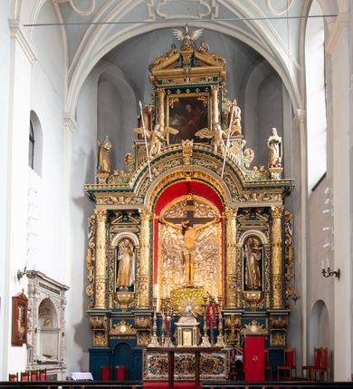 Zdjęcie nr 14: Ołtarz architektoniczny, trójosiowy, dwukondygnacyjny ze zwieńczeniem. Mensa prostopadłościenna, kamienna z drewnianym antepedium w formie leżącego prostokąta z postacią św. Augustyna ujętego wicią suchego akantu z przeplecioną, karbowaną wstążką i bukietami kwiatów. Przedstawienie otoczone profilowaną, ażurową ramą wypełnioną podobną wicią z akantu i kwiatów. Na mensie prostopadłościenne tabernakulum w formie kapliczki. Ściana frontowa z drzwiczkami w kształcie stojącego prostokąta dekorowanego krzyżem łacińskim ujętym wicią roślinną, zwieńczona trójkątnym przyczółkiem. Ścianka ujęta lizenami wypełnionymi wicią akantową podtrzymującymi pełne belkowanie obiegające bryłę, z mocno wysuniętym gzymsem wyłamanym w narożach. Całość zwieńczona czterospadowym dachem dekorowanym łuską. Na dachu baranek Boży leżący na księdze z siedmioma pieczęciami, przytrzymujący chorągiew, ukazany na tle chrystogramu otoczonego glorią promienistą. 
Nastawa na dwudzielnym cokole z półkolistymi bramkami ze zwieńczeniem utworzonym z ornamentu okuciowego ujmującego owalne pola. Osie pierwszej kondygnacji wydzielone kolumnami stojącymi na konsolach dekorowanych z frontu uskrzydlonymi główkami anielskimi powyżej liści akantu, na krawędziach cekinami, a po bokach wicią. Kolumny zostały przedzielone opaską w jednej trzeciej wysokości, dekorowane na całej wysokości wicią roślinną, główkami anielskimi w dolnej partii i imitacją kameryzacji na opaskach oraz w dwóch trzecich wysokości. Kolumny są ustawione na tle pilastrów dekorowanych wicią roślinną i zawieszonymi na niej chustkami. W polu centralnym kondygnacji jest nisza w kształcie stojącego prostokąta zamkniętego łukiem pełnym z postacią ukrzyżowanego Chrystusa na tle widoku Jerozolimy. W osiach bocznych mniejsze, ujęte pilastrami nisze o podobnym kształcie, których konchy wypełnione są muszlą, zwieńczone trójkątnym przyczółkiem przerwanym na cokół. W nich, na dekorowanych wicią i rozetami konsolach ustawiono figury: po lewej stronie św. Piotra, a po prawej św. Pawła. Kondygnacje ujmują ażurowe uszaki utworzone z ornamentu okuciowego, ulistnionych wolut i przewieszonej chustki. Kolumny podtrzymują pełne belkowanie wyniesione w łuk nad polem centralnym. Podłucze dekorowane rozetami, fryz głowami anielskimi i wicią, gzyms m.in. kostkowaniem i liśćmi akantu. Całość spięta kluczem z kartuszem z herbem kanoników regularnych od pokuty (marków). Na wyniesieniu belkowania posadowiono postaci aniołów trzymających narzędzia męki: anioł po lewej włócznię, a anioł po prawej gąbkę. Górna kondygnacja oparta została na schemacie aediculi – prostokątne pole ujęto kolumnami podtrzymującymi pełne belkowanie i trójkątny przyczółek przerwany na środku na cokół, na którym ustawiono rzeźbę  pelikana karmiącego młode własną krwią. Na krawędziach przyczółka dwie leżące postaci. Kondygnacja flankowana postaciami czterech ewangelistów ustawionymi na cokołach. Po lewej stronie św. Marek i św. Jan, po prawej św. Mateusz i św. Łukasz. Struktura polichromowana na kolor ciemnoniebieski; kolumny, profile, detale i ornamenty złocone i srebrzone.
