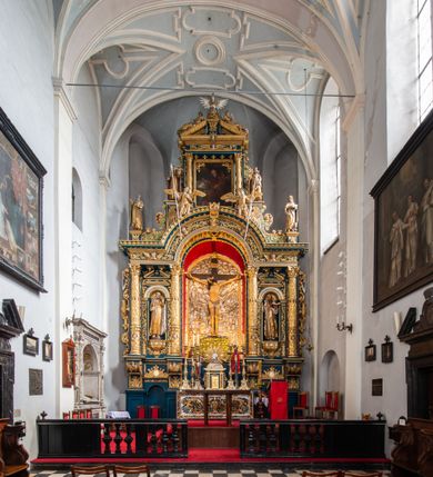 Zdjęcie nr 3: Ołtarz architektoniczny, trójosiowy, dwukondygnacyjny ze zwieńczeniem. Mensa prostopadłościenna, kamienna z drewnianym antepedium w formie leżącego prostokąta z postacią św. Augustyna ujętego wicią suchego akantu z przeplecioną, karbowaną wstążką i bukietami kwiatów. Przedstawienie otoczone profilowaną, ażurową ramą wypełnioną podobną wicią z akantu i kwiatów. Na mensie prostopadłościenne tabernakulum w formie kapliczki. Ściana frontowa z drzwiczkami w kształcie stojącego prostokąta dekorowanego krzyżem łacińskim ujętym wicią roślinną, zwieńczona trójkątnym przyczółkiem. Ścianka ujęta lizenami wypełnionymi wicią akantową podtrzymującymi pełne belkowanie obiegające bryłę, z mocno wysuniętym gzymsem wyłamanym w narożach. Całość zwieńczona czterospadowym dachem dekorowanym łuską. Na dachu baranek Boży leżący na księdze z siedmioma pieczęciami, przytrzymujący chorągiew, ukazany na tle chrystogramu otoczonego glorią promienistą. 
Nastawa na dwudzielnym cokole z półkolistymi bramkami ze zwieńczeniem utworzonym z ornamentu okuciowego ujmującego owalne pola. Osie pierwszej kondygnacji wydzielone kolumnami stojącymi na konsolach dekorowanych z frontu uskrzydlonymi główkami anielskimi powyżej liści akantu, na krawędziach cekinami, a po bokach wicią. Kolumny zostały przedzielone opaską w jednej trzeciej wysokości, dekorowane na całej wysokości wicią roślinną, główkami anielskimi w dolnej partii i imitacją kameryzacji na opaskach oraz w dwóch trzecich wysokości. Kolumny są ustawione na tle pilastrów dekorowanych wicią roślinną i zawieszonymi na niej chustkami. W polu centralnym kondygnacji jest nisza w kształcie stojącego prostokąta zamkniętego łukiem pełnym z postacią ukrzyżowanego Chrystusa na tle widoku Jerozolimy. W osiach bocznych mniejsze, ujęte pilastrami nisze o podobnym kształcie, których konchy wypełnione są muszlą, zwieńczone trójkątnym przyczółkiem przerwanym na cokół. W nich, na dekorowanych wicią i rozetami konsolach ustawiono figury: po lewej stronie św. Piotra, a po prawej św. Pawła. Kondygnacje ujmują ażurowe uszaki utworzone z ornamentu okuciowego, ulistnionych wolut i przewieszonej chustki. Kolumny podtrzymują pełne belkowanie wyniesione w łuk nad polem centralnym. Podłucze dekorowane rozetami, fryz głowami anielskimi i wicią, gzyms m.in. kostkowaniem i liśćmi akantu. Całość spięta kluczem z kartuszem z herbem kanoników regularnych od pokuty (marków). Na wyniesieniu belkowania posadowiono postaci aniołów trzymających narzędzia męki: anioł po lewej włócznię, a anioł po prawej gąbkę. Górna kondygnacja oparta została na schemacie aediculi – prostokątne pole ujęto kolumnami podtrzymującymi pełne belkowanie i trójkątny przyczółek przerwany na środku na cokół, na którym ustawiono rzeźbę  pelikana karmiącego młode własną krwią. Na krawędziach przyczółka dwie leżące postaci. Kondygnacja flankowana postaciami czterech ewangelistów ustawionymi na cokołach. Po lewej stronie św. Marek i św. Jan, po prawej św. Mateusz i św. Łukasz. Struktura polichromowana na kolor ciemnoniebieski; kolumny, profile, detale i ornamenty złocone i srebrzone.
