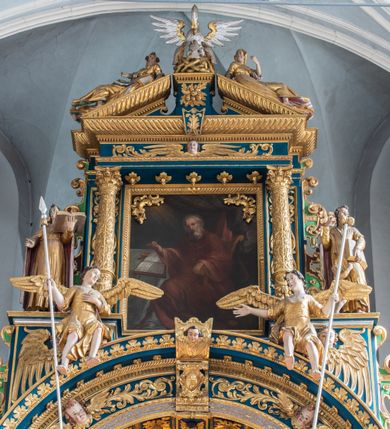 Zdjęcie nr 36: Ołtarz architektoniczny, trójosiowy, dwukondygnacyjny ze zwieńczeniem. Mensa prostopadłościenna, kamienna z drewnianym antepedium w formie leżącego prostokąta z postacią św. Augustyna ujętego wicią suchego akantu z przeplecioną, karbowaną wstążką i bukietami kwiatów. Przedstawienie otoczone profilowaną, ażurową ramą wypełnioną podobną wicią z akantu i kwiatów. Na mensie prostopadłościenne tabernakulum w formie kapliczki. Ściana frontowa z drzwiczkami w kształcie stojącego prostokąta dekorowanego krzyżem łacińskim ujętym wicią roślinną, zwieńczona trójkątnym przyczółkiem. Ścianka ujęta lizenami wypełnionymi wicią akantową podtrzymującymi pełne belkowanie obiegające bryłę, z mocno wysuniętym gzymsem wyłamanym w narożach. Całość zwieńczona czterospadowym dachem dekorowanym łuską. Na dachu baranek Boży leżący na księdze z siedmioma pieczęciami, przytrzymujący chorągiew, ukazany na tle chrystogramu otoczonego glorią promienistą. 
Nastawa na dwudzielnym cokole z półkolistymi bramkami ze zwieńczeniem utworzonym z ornamentu okuciowego ujmującego owalne pola. Osie pierwszej kondygnacji wydzielone kolumnami stojącymi na konsolach dekorowanych z frontu uskrzydlonymi główkami anielskimi powyżej liści akantu, na krawędziach cekinami, a po bokach wicią. Kolumny zostały przedzielone opaską w jednej trzeciej wysokości, dekorowane na całej wysokości wicią roślinną, główkami anielskimi w dolnej partii i imitacją kameryzacji na opaskach oraz w dwóch trzecich wysokości. Kolumny są ustawione na tle pilastrów dekorowanych wicią roślinną i zawieszonymi na niej chustkami. W polu centralnym kondygnacji jest nisza w kształcie stojącego prostokąta zamkniętego łukiem pełnym z postacią ukrzyżowanego Chrystusa na tle widoku Jerozolimy. W osiach bocznych mniejsze, ujęte pilastrami nisze o podobnym kształcie, których konchy wypełnione są muszlą, zwieńczone trójkątnym przyczółkiem przerwanym na cokół. W nich, na dekorowanych wicią i rozetami konsolach ustawiono figury: po lewej stronie św. Piotra, a po prawej św. Pawła. Kondygnacje ujmują ażurowe uszaki utworzone z ornamentu okuciowego, ulistnionych wolut i przewieszonej chustki. Kolumny podtrzymują pełne belkowanie wyniesione w łuk nad polem centralnym. Podłucze dekorowane rozetami, fryz głowami anielskimi i wicią, gzyms m.in. kostkowaniem i liśćmi akantu. Całość spięta kluczem z kartuszem z herbem kanoników regularnych od pokuty (marków). Na wyniesieniu belkowania posadowiono postaci aniołów trzymających narzędzia męki: anioł po lewej włócznię, a anioł po prawej gąbkę. Górna kondygnacja oparta została na schemacie aediculi – prostokątne pole ujęto kolumnami podtrzymującymi pełne belkowanie i trójkątny przyczółek przerwany na środku na cokół, na którym ustawiono rzeźbę  pelikana karmiącego młode własną krwią. Na krawędziach przyczółka dwie leżące postaci. Kondygnacja flankowana postaciami czterech ewangelistów ustawionymi na cokołach. Po lewej stronie św. Marek i św. Jan, po prawej św. Mateusz i św. Łukasz. Struktura polichromowana na kolor ciemnoniebieski; kolumny, profile, detale i ornamenty złocone i srebrzone.
