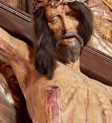 Zdjęcie nr 46: Ołtarz architektoniczny, trójosiowy, dwukondygnacyjny ze zwieńczeniem. Mensa prostopadłościenna, kamienna z drewnianym antepedium w formie leżącego prostokąta z postacią św. Augustyna ujętego wicią suchego akantu z przeplecioną, karbowaną wstążką i bukietami kwiatów. Przedstawienie otoczone profilowaną, ażurową ramą wypełnioną podobną wicią z akantu i kwiatów. Na mensie prostopadłościenne tabernakulum w formie kapliczki. Ściana frontowa z drzwiczkami w kształcie stojącego prostokąta dekorowanego krzyżem łacińskim ujętym wicią roślinną, zwieńczona trójkątnym przyczółkiem. Ścianka ujęta lizenami wypełnionymi wicią akantową podtrzymującymi pełne belkowanie obiegające bryłę, z mocno wysuniętym gzymsem wyłamanym w narożach. Całość zwieńczona czterospadowym dachem dekorowanym łuską. Na dachu baranek Boży leżący na księdze z siedmioma pieczęciami, przytrzymujący chorągiew, ukazany na tle chrystogramu otoczonego glorią promienistą. 
Nastawa na dwudzielnym cokole z półkolistymi bramkami ze zwieńczeniem utworzonym z ornamentu okuciowego ujmującego owalne pola. Osie pierwszej kondygnacji wydzielone kolumnami stojącymi na konsolach dekorowanych z frontu uskrzydlonymi główkami anielskimi powyżej liści akantu, na krawędziach cekinami, a po bokach wicią. Kolumny zostały przedzielone opaską w jednej trzeciej wysokości, dekorowane na całej wysokości wicią roślinną, główkami anielskimi w dolnej partii i imitacją kameryzacji na opaskach oraz w dwóch trzecich wysokości. Kolumny są ustawione na tle pilastrów dekorowanych wicią roślinną i zawieszonymi na niej chustkami. W polu centralnym kondygnacji jest nisza w kształcie stojącego prostokąta zamkniętego łukiem pełnym z postacią ukrzyżowanego Chrystusa na tle widoku Jerozolimy. W osiach bocznych mniejsze, ujęte pilastrami nisze o podobnym kształcie, których konchy wypełnione są muszlą, zwieńczone trójkątnym przyczółkiem przerwanym na cokół. W nich, na dekorowanych wicią i rozetami konsolach ustawiono figury: po lewej stronie św. Piotra, a po prawej św. Pawła. Kondygnacje ujmują ażurowe uszaki utworzone z ornamentu okuciowego, ulistnionych wolut i przewieszonej chustki. Kolumny podtrzymują pełne belkowanie wyniesione w łuk nad polem centralnym. Podłucze dekorowane rozetami, fryz głowami anielskimi i wicią, gzyms m.in. kostkowaniem i liśćmi akantu. Całość spięta kluczem z kartuszem z herbem kanoników regularnych od pokuty (marków). Na wyniesieniu belkowania posadowiono postaci aniołów trzymających narzędzia męki: anioł po lewej włócznię, a anioł po prawej gąbkę. Górna kondygnacja oparta została na schemacie aediculi – prostokątne pole ujęto kolumnami podtrzymującymi pełne belkowanie i trójkątny przyczółek przerwany na środku na cokół, na którym ustawiono rzeźbę  pelikana karmiącego młode własną krwią. Na krawędziach przyczółka dwie leżące postaci. Kondygnacja flankowana postaciami czterech ewangelistów ustawionymi na cokołach. Po lewej stronie św. Marek i św. Jan, po prawej św. Mateusz i św. Łukasz. Struktura polichromowana na kolor ciemnoniebieski; kolumny, profile, detale i ornamenty złocone i srebrzone.
