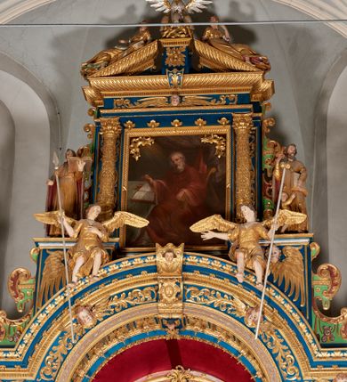 Zdjęcie nr 49: Ołtarz architektoniczny, trójosiowy, dwukondygnacyjny ze zwieńczeniem. Mensa prostopadłościenna, kamienna z drewnianym antepedium w formie leżącego prostokąta z postacią św. Augustyna ujętego wicią suchego akantu z przeplecioną, karbowaną wstążką i bukietami kwiatów. Przedstawienie otoczone profilowaną, ażurową ramą wypełnioną podobną wicią z akantu i kwiatów. Na mensie prostopadłościenne tabernakulum w formie kapliczki. Ściana frontowa z drzwiczkami w kształcie stojącego prostokąta dekorowanego krzyżem łacińskim ujętym wicią roślinną, zwieńczona trójkątnym przyczółkiem. Ścianka ujęta lizenami wypełnionymi wicią akantową podtrzymującymi pełne belkowanie obiegające bryłę, z mocno wysuniętym gzymsem wyłamanym w narożach. Całość zwieńczona czterospadowym dachem dekorowanym łuską. Na dachu baranek Boży leżący na księdze z siedmioma pieczęciami, przytrzymujący chorągiew, ukazany na tle chrystogramu otoczonego glorią promienistą. 
Nastawa na dwudzielnym cokole z półkolistymi bramkami ze zwieńczeniem utworzonym z ornamentu okuciowego ujmującego owalne pola. Osie pierwszej kondygnacji wydzielone kolumnami stojącymi na konsolach dekorowanych z frontu uskrzydlonymi główkami anielskimi powyżej liści akantu, na krawędziach cekinami, a po bokach wicią. Kolumny zostały przedzielone opaską w jednej trzeciej wysokości, dekorowane na całej wysokości wicią roślinną, główkami anielskimi w dolnej partii i imitacją kameryzacji na opaskach oraz w dwóch trzecich wysokości. Kolumny są ustawione na tle pilastrów dekorowanych wicią roślinną i zawieszonymi na niej chustkami. W polu centralnym kondygnacji jest nisza w kształcie stojącego prostokąta zamkniętego łukiem pełnym z postacią ukrzyżowanego Chrystusa na tle widoku Jerozolimy. W osiach bocznych mniejsze, ujęte pilastrami nisze o podobnym kształcie, których konchy wypełnione są muszlą, zwieńczone trójkątnym przyczółkiem przerwanym na cokół. W nich, na dekorowanych wicią i rozetami konsolach ustawiono figury: po lewej stronie św. Piotra, a po prawej św. Pawła. Kondygnacje ujmują ażurowe uszaki utworzone z ornamentu okuciowego, ulistnionych wolut i przewieszonej chustki. Kolumny podtrzymują pełne belkowanie wyniesione w łuk nad polem centralnym. Podłucze dekorowane rozetami, fryz głowami anielskimi i wicią, gzyms m.in. kostkowaniem i liśćmi akantu. Całość spięta kluczem z kartuszem z herbem kanoników regularnych od pokuty (marków). Na wyniesieniu belkowania posadowiono postaci aniołów trzymających narzędzia męki: anioł po lewej włócznię, a anioł po prawej gąbkę. Górna kondygnacja oparta została na schemacie aediculi – prostokątne pole ujęto kolumnami podtrzymującymi pełne belkowanie i trójkątny przyczółek przerwany na środku na cokół, na którym ustawiono rzeźbę  pelikana karmiącego młode własną krwią. Na krawędziach przyczółka dwie leżące postaci. Kondygnacja flankowana postaciami czterech ewangelistów ustawionymi na cokołach. Po lewej stronie św. Marek i św. Jan, po prawej św. Mateusz i św. Łukasz. Struktura polichromowana na kolor ciemnoniebieski; kolumny, profile, detale i ornamenty złocone i srebrzone.
