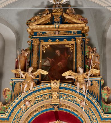 Zdjęcie nr 50: Ołtarz architektoniczny, trójosiowy, dwukondygnacyjny ze zwieńczeniem. Mensa prostopadłościenna, kamienna z drewnianym antepedium w formie leżącego prostokąta z postacią św. Augustyna ujętego wicią suchego akantu z przeplecioną, karbowaną wstążką i bukietami kwiatów. Przedstawienie otoczone profilowaną, ażurową ramą wypełnioną podobną wicią z akantu i kwiatów. Na mensie prostopadłościenne tabernakulum w formie kapliczki. Ściana frontowa z drzwiczkami w kształcie stojącego prostokąta dekorowanego krzyżem łacińskim ujętym wicią roślinną, zwieńczona trójkątnym przyczółkiem. Ścianka ujęta lizenami wypełnionymi wicią akantową podtrzymującymi pełne belkowanie obiegające bryłę, z mocno wysuniętym gzymsem wyłamanym w narożach. Całość zwieńczona czterospadowym dachem dekorowanym łuską. Na dachu baranek Boży leżący na księdze z siedmioma pieczęciami, przytrzymujący chorągiew, ukazany na tle chrystogramu otoczonego glorią promienistą. 
Nastawa na dwudzielnym cokole z półkolistymi bramkami ze zwieńczeniem utworzonym z ornamentu okuciowego ujmującego owalne pola. Osie pierwszej kondygnacji wydzielone kolumnami stojącymi na konsolach dekorowanych z frontu uskrzydlonymi główkami anielskimi powyżej liści akantu, na krawędziach cekinami, a po bokach wicią. Kolumny zostały przedzielone opaską w jednej trzeciej wysokości, dekorowane na całej wysokości wicią roślinną, główkami anielskimi w dolnej partii i imitacją kameryzacji na opaskach oraz w dwóch trzecich wysokości. Kolumny są ustawione na tle pilastrów dekorowanych wicią roślinną i zawieszonymi na niej chustkami. W polu centralnym kondygnacji jest nisza w kształcie stojącego prostokąta zamkniętego łukiem pełnym z postacią ukrzyżowanego Chrystusa na tle widoku Jerozolimy. W osiach bocznych mniejsze, ujęte pilastrami nisze o podobnym kształcie, których konchy wypełnione są muszlą, zwieńczone trójkątnym przyczółkiem przerwanym na cokół. W nich, na dekorowanych wicią i rozetami konsolach ustawiono figury: po lewej stronie św. Piotra, a po prawej św. Pawła. Kondygnacje ujmują ażurowe uszaki utworzone z ornamentu okuciowego, ulistnionych wolut i przewieszonej chustki. Kolumny podtrzymują pełne belkowanie wyniesione w łuk nad polem centralnym. Podłucze dekorowane rozetami, fryz głowami anielskimi i wicią, gzyms m.in. kostkowaniem i liśćmi akantu. Całość spięta kluczem z kartuszem z herbem kanoników regularnych od pokuty (marków). Na wyniesieniu belkowania posadowiono postaci aniołów trzymających narzędzia męki: anioł po lewej włócznię, a anioł po prawej gąbkę. Górna kondygnacja oparta została na schemacie aediculi – prostokątne pole ujęto kolumnami podtrzymującymi pełne belkowanie i trójkątny przyczółek przerwany na środku na cokół, na którym ustawiono rzeźbę  pelikana karmiącego młode własną krwią. Na krawędziach przyczółka dwie leżące postaci. Kondygnacja flankowana postaciami czterech ewangelistów ustawionymi na cokołach. Po lewej stronie św. Marek i św. Jan, po prawej św. Mateusz i św. Łukasz. Struktura polichromowana na kolor ciemnoniebieski; kolumny, profile, detale i ornamenty złocone i srebrzone.
