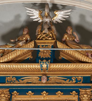 Zdjęcie nr 51: Ołtarz architektoniczny, trójosiowy, dwukondygnacyjny ze zwieńczeniem. Mensa prostopadłościenna, kamienna z drewnianym antepedium w formie leżącego prostokąta z postacią św. Augustyna ujętego wicią suchego akantu z przeplecioną, karbowaną wstążką i bukietami kwiatów. Przedstawienie otoczone profilowaną, ażurową ramą wypełnioną podobną wicią z akantu i kwiatów. Na mensie prostopadłościenne tabernakulum w formie kapliczki. Ściana frontowa z drzwiczkami w kształcie stojącego prostokąta dekorowanego krzyżem łacińskim ujętym wicią roślinną, zwieńczona trójkątnym przyczółkiem. Ścianka ujęta lizenami wypełnionymi wicią akantową podtrzymującymi pełne belkowanie obiegające bryłę, z mocno wysuniętym gzymsem wyłamanym w narożach. Całość zwieńczona czterospadowym dachem dekorowanym łuską. Na dachu baranek Boży leżący na księdze z siedmioma pieczęciami, przytrzymujący chorągiew, ukazany na tle chrystogramu otoczonego glorią promienistą. 
Nastawa na dwudzielnym cokole z półkolistymi bramkami ze zwieńczeniem utworzonym z ornamentu okuciowego ujmującego owalne pola. Osie pierwszej kondygnacji wydzielone kolumnami stojącymi na konsolach dekorowanych z frontu uskrzydlonymi główkami anielskimi powyżej liści akantu, na krawędziach cekinami, a po bokach wicią. Kolumny zostały przedzielone opaską w jednej trzeciej wysokości, dekorowane na całej wysokości wicią roślinną, główkami anielskimi w dolnej partii i imitacją kameryzacji na opaskach oraz w dwóch trzecich wysokości. Kolumny są ustawione na tle pilastrów dekorowanych wicią roślinną i zawieszonymi na niej chustkami. W polu centralnym kondygnacji jest nisza w kształcie stojącego prostokąta zamkniętego łukiem pełnym z postacią ukrzyżowanego Chrystusa na tle widoku Jerozolimy. W osiach bocznych mniejsze, ujęte pilastrami nisze o podobnym kształcie, których konchy wypełnione są muszlą, zwieńczone trójkątnym przyczółkiem przerwanym na cokół. W nich, na dekorowanych wicią i rozetami konsolach ustawiono figury: po lewej stronie św. Piotra, a po prawej św. Pawła. Kondygnacje ujmują ażurowe uszaki utworzone z ornamentu okuciowego, ulistnionych wolut i przewieszonej chustki. Kolumny podtrzymują pełne belkowanie wyniesione w łuk nad polem centralnym. Podłucze dekorowane rozetami, fryz głowami anielskimi i wicią, gzyms m.in. kostkowaniem i liśćmi akantu. Całość spięta kluczem z kartuszem z herbem kanoników regularnych od pokuty (marków). Na wyniesieniu belkowania posadowiono postaci aniołów trzymających narzędzia męki: anioł po lewej włócznię, a anioł po prawej gąbkę. Górna kondygnacja oparta została na schemacie aediculi – prostokątne pole ujęto kolumnami podtrzymującymi pełne belkowanie i trójkątny przyczółek przerwany na środku na cokół, na którym ustawiono rzeźbę  pelikana karmiącego młode własną krwią. Na krawędziach przyczółka dwie leżące postaci. Kondygnacja flankowana postaciami czterech ewangelistów ustawionymi na cokołach. Po lewej stronie św. Marek i św. Jan, po prawej św. Mateusz i św. Łukasz. Struktura polichromowana na kolor ciemnoniebieski; kolumny, profile, detale i ornamenty złocone i srebrzone.
