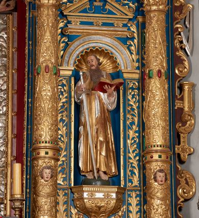 Zdjęcie nr 53: Ołtarz architektoniczny, trójosiowy, dwukondygnacyjny ze zwieńczeniem. Mensa prostopadłościenna, kamienna z drewnianym antepedium w formie leżącego prostokąta z postacią św. Augustyna ujętego wicią suchego akantu z przeplecioną, karbowaną wstążką i bukietami kwiatów. Przedstawienie otoczone profilowaną, ażurową ramą wypełnioną podobną wicią z akantu i kwiatów. Na mensie prostopadłościenne tabernakulum w formie kapliczki. Ściana frontowa z drzwiczkami w kształcie stojącego prostokąta dekorowanego krzyżem łacińskim ujętym wicią roślinną, zwieńczona trójkątnym przyczółkiem. Ścianka ujęta lizenami wypełnionymi wicią akantową podtrzymującymi pełne belkowanie obiegające bryłę, z mocno wysuniętym gzymsem wyłamanym w narożach. Całość zwieńczona czterospadowym dachem dekorowanym łuską. Na dachu baranek Boży leżący na księdze z siedmioma pieczęciami, przytrzymujący chorągiew, ukazany na tle chrystogramu otoczonego glorią promienistą. 
Nastawa na dwudzielnym cokole z półkolistymi bramkami ze zwieńczeniem utworzonym z ornamentu okuciowego ujmującego owalne pola. Osie pierwszej kondygnacji wydzielone kolumnami stojącymi na konsolach dekorowanych z frontu uskrzydlonymi główkami anielskimi powyżej liści akantu, na krawędziach cekinami, a po bokach wicią. Kolumny zostały przedzielone opaską w jednej trzeciej wysokości, dekorowane na całej wysokości wicią roślinną, główkami anielskimi w dolnej partii i imitacją kameryzacji na opaskach oraz w dwóch trzecich wysokości. Kolumny są ustawione na tle pilastrów dekorowanych wicią roślinną i zawieszonymi na niej chustkami. W polu centralnym kondygnacji jest nisza w kształcie stojącego prostokąta zamkniętego łukiem pełnym z postacią ukrzyżowanego Chrystusa na tle widoku Jerozolimy. W osiach bocznych mniejsze, ujęte pilastrami nisze o podobnym kształcie, których konchy wypełnione są muszlą, zwieńczone trójkątnym przyczółkiem przerwanym na cokół. W nich, na dekorowanych wicią i rozetami konsolach ustawiono figury: po lewej stronie św. Piotra, a po prawej św. Pawła. Kondygnacje ujmują ażurowe uszaki utworzone z ornamentu okuciowego, ulistnionych wolut i przewieszonej chustki. Kolumny podtrzymują pełne belkowanie wyniesione w łuk nad polem centralnym. Podłucze dekorowane rozetami, fryz głowami anielskimi i wicią, gzyms m.in. kostkowaniem i liśćmi akantu. Całość spięta kluczem z kartuszem z herbem kanoników regularnych od pokuty (marków). Na wyniesieniu belkowania posadowiono postaci aniołów trzymających narzędzia męki: anioł po lewej włócznię, a anioł po prawej gąbkę. Górna kondygnacja oparta została na schemacie aediculi – prostokątne pole ujęto kolumnami podtrzymującymi pełne belkowanie i trójkątny przyczółek przerwany na środku na cokół, na którym ustawiono rzeźbę  pelikana karmiącego młode własną krwią. Na krawędziach przyczółka dwie leżące postaci. Kondygnacja flankowana postaciami czterech ewangelistów ustawionymi na cokołach. Po lewej stronie św. Marek i św. Jan, po prawej św. Mateusz i św. Łukasz. Struktura polichromowana na kolor ciemnoniebieski; kolumny, profile, detale i ornamenty złocone i srebrzone.
