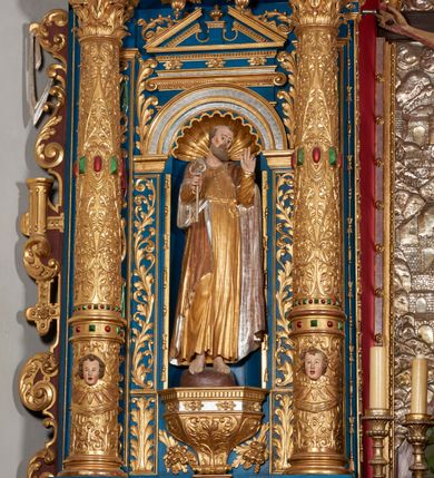 Zdjęcie nr 54: Ołtarz architektoniczny, trójosiowy, dwukondygnacyjny ze zwieńczeniem. Mensa prostopadłościenna, kamienna z drewnianym antepedium w formie leżącego prostokąta z postacią św. Augustyna ujętego wicią suchego akantu z przeplecioną, karbowaną wstążką i bukietami kwiatów. Przedstawienie otoczone profilowaną, ażurową ramą wypełnioną podobną wicią z akantu i kwiatów. Na mensie prostopadłościenne tabernakulum w formie kapliczki. Ściana frontowa z drzwiczkami w kształcie stojącego prostokąta dekorowanego krzyżem łacińskim ujętym wicią roślinną, zwieńczona trójkątnym przyczółkiem. Ścianka ujęta lizenami wypełnionymi wicią akantową podtrzymującymi pełne belkowanie obiegające bryłę, z mocno wysuniętym gzymsem wyłamanym w narożach. Całość zwieńczona czterospadowym dachem dekorowanym łuską. Na dachu baranek Boży leżący na księdze z siedmioma pieczęciami, przytrzymujący chorągiew, ukazany na tle chrystogramu otoczonego glorią promienistą. 
Nastawa na dwudzielnym cokole z półkolistymi bramkami ze zwieńczeniem utworzonym z ornamentu okuciowego ujmującego owalne pola. Osie pierwszej kondygnacji wydzielone kolumnami stojącymi na konsolach dekorowanych z frontu uskrzydlonymi główkami anielskimi powyżej liści akantu, na krawędziach cekinami, a po bokach wicią. Kolumny zostały przedzielone opaską w jednej trzeciej wysokości, dekorowane na całej wysokości wicią roślinną, główkami anielskimi w dolnej partii i imitacją kameryzacji na opaskach oraz w dwóch trzecich wysokości. Kolumny są ustawione na tle pilastrów dekorowanych wicią roślinną i zawieszonymi na niej chustkami. W polu centralnym kondygnacji jest nisza w kształcie stojącego prostokąta zamkniętego łukiem pełnym z postacią ukrzyżowanego Chrystusa na tle widoku Jerozolimy. W osiach bocznych mniejsze, ujęte pilastrami nisze o podobnym kształcie, których konchy wypełnione są muszlą, zwieńczone trójkątnym przyczółkiem przerwanym na cokół. W nich, na dekorowanych wicią i rozetami konsolach ustawiono figury: po lewej stronie św. Piotra, a po prawej św. Pawła. Kondygnacje ujmują ażurowe uszaki utworzone z ornamentu okuciowego, ulistnionych wolut i przewieszonej chustki. Kolumny podtrzymują pełne belkowanie wyniesione w łuk nad polem centralnym. Podłucze dekorowane rozetami, fryz głowami anielskimi i wicią, gzyms m.in. kostkowaniem i liśćmi akantu. Całość spięta kluczem z kartuszem z herbem kanoników regularnych od pokuty (marków). Na wyniesieniu belkowania posadowiono postaci aniołów trzymających narzędzia męki: anioł po lewej włócznię, a anioł po prawej gąbkę. Górna kondygnacja oparta została na schemacie aediculi – prostokątne pole ujęto kolumnami podtrzymującymi pełne belkowanie i trójkątny przyczółek przerwany na środku na cokół, na którym ustawiono rzeźbę  pelikana karmiącego młode własną krwią. Na krawędziach przyczółka dwie leżące postaci. Kondygnacja flankowana postaciami czterech ewangelistów ustawionymi na cokołach. Po lewej stronie św. Marek i św. Jan, po prawej św. Mateusz i św. Łukasz. Struktura polichromowana na kolor ciemnoniebieski; kolumny, profile, detale i ornamenty złocone i srebrzone.
