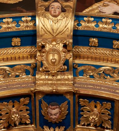 Zdjęcie nr 55: Ołtarz architektoniczny, trójosiowy, dwukondygnacyjny ze zwieńczeniem. Mensa prostopadłościenna, kamienna z drewnianym antepedium w formie leżącego prostokąta z postacią św. Augustyna ujętego wicią suchego akantu z przeplecioną, karbowaną wstążką i bukietami kwiatów. Przedstawienie otoczone profilowaną, ażurową ramą wypełnioną podobną wicią z akantu i kwiatów. Na mensie prostopadłościenne tabernakulum w formie kapliczki. Ściana frontowa z drzwiczkami w kształcie stojącego prostokąta dekorowanego krzyżem łacińskim ujętym wicią roślinną, zwieńczona trójkątnym przyczółkiem. Ścianka ujęta lizenami wypełnionymi wicią akantową podtrzymującymi pełne belkowanie obiegające bryłę, z mocno wysuniętym gzymsem wyłamanym w narożach. Całość zwieńczona czterospadowym dachem dekorowanym łuską. Na dachu baranek Boży leżący na księdze z siedmioma pieczęciami, przytrzymujący chorągiew, ukazany na tle chrystogramu otoczonego glorią promienistą. 
Nastawa na dwudzielnym cokole z półkolistymi bramkami ze zwieńczeniem utworzonym z ornamentu okuciowego ujmującego owalne pola. Osie pierwszej kondygnacji wydzielone kolumnami stojącymi na konsolach dekorowanych z frontu uskrzydlonymi główkami anielskimi powyżej liści akantu, na krawędziach cekinami, a po bokach wicią. Kolumny zostały przedzielone opaską w jednej trzeciej wysokości, dekorowane na całej wysokości wicią roślinną, główkami anielskimi w dolnej partii i imitacją kameryzacji na opaskach oraz w dwóch trzecich wysokości. Kolumny są ustawione na tle pilastrów dekorowanych wicią roślinną i zawieszonymi na niej chustkami. W polu centralnym kondygnacji jest nisza w kształcie stojącego prostokąta zamkniętego łukiem pełnym z postacią ukrzyżowanego Chrystusa na tle widoku Jerozolimy. W osiach bocznych mniejsze, ujęte pilastrami nisze o podobnym kształcie, których konchy wypełnione są muszlą, zwieńczone trójkątnym przyczółkiem przerwanym na cokół. W nich, na dekorowanych wicią i rozetami konsolach ustawiono figury: po lewej stronie św. Piotra, a po prawej św. Pawła. Kondygnacje ujmują ażurowe uszaki utworzone z ornamentu okuciowego, ulistnionych wolut i przewieszonej chustki. Kolumny podtrzymują pełne belkowanie wyniesione w łuk nad polem centralnym. Podłucze dekorowane rozetami, fryz głowami anielskimi i wicią, gzyms m.in. kostkowaniem i liśćmi akantu. Całość spięta kluczem z kartuszem z herbem kanoników regularnych od pokuty (marków). Na wyniesieniu belkowania posadowiono postaci aniołów trzymających narzędzia męki: anioł po lewej włócznię, a anioł po prawej gąbkę. Górna kondygnacja oparta została na schemacie aediculi – prostokątne pole ujęto kolumnami podtrzymującymi pełne belkowanie i trójkątny przyczółek przerwany na środku na cokół, na którym ustawiono rzeźbę  pelikana karmiącego młode własną krwią. Na krawędziach przyczółka dwie leżące postaci. Kondygnacja flankowana postaciami czterech ewangelistów ustawionymi na cokołach. Po lewej stronie św. Marek i św. Jan, po prawej św. Mateusz i św. Łukasz. Struktura polichromowana na kolor ciemnoniebieski; kolumny, profile, detale i ornamenty złocone i srebrzone.
