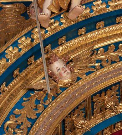 Zdjęcie nr 56: Ołtarz architektoniczny, trójosiowy, dwukondygnacyjny ze zwieńczeniem. Mensa prostopadłościenna, kamienna z drewnianym antepedium w formie leżącego prostokąta z postacią św. Augustyna ujętego wicią suchego akantu z przeplecioną, karbowaną wstążką i bukietami kwiatów. Przedstawienie otoczone profilowaną, ażurową ramą wypełnioną podobną wicią z akantu i kwiatów. Na mensie prostopadłościenne tabernakulum w formie kapliczki. Ściana frontowa z drzwiczkami w kształcie stojącego prostokąta dekorowanego krzyżem łacińskim ujętym wicią roślinną, zwieńczona trójkątnym przyczółkiem. Ścianka ujęta lizenami wypełnionymi wicią akantową podtrzymującymi pełne belkowanie obiegające bryłę, z mocno wysuniętym gzymsem wyłamanym w narożach. Całość zwieńczona czterospadowym dachem dekorowanym łuską. Na dachu baranek Boży leżący na księdze z siedmioma pieczęciami, przytrzymujący chorągiew, ukazany na tle chrystogramu otoczonego glorią promienistą. 
Nastawa na dwudzielnym cokole z półkolistymi bramkami ze zwieńczeniem utworzonym z ornamentu okuciowego ujmującego owalne pola. Osie pierwszej kondygnacji wydzielone kolumnami stojącymi na konsolach dekorowanych z frontu uskrzydlonymi główkami anielskimi powyżej liści akantu, na krawędziach cekinami, a po bokach wicią. Kolumny zostały przedzielone opaską w jednej trzeciej wysokości, dekorowane na całej wysokości wicią roślinną, główkami anielskimi w dolnej partii i imitacją kameryzacji na opaskach oraz w dwóch trzecich wysokości. Kolumny są ustawione na tle pilastrów dekorowanych wicią roślinną i zawieszonymi na niej chustkami. W polu centralnym kondygnacji jest nisza w kształcie stojącego prostokąta zamkniętego łukiem pełnym z postacią ukrzyżowanego Chrystusa na tle widoku Jerozolimy. W osiach bocznych mniejsze, ujęte pilastrami nisze o podobnym kształcie, których konchy wypełnione są muszlą, zwieńczone trójkątnym przyczółkiem przerwanym na cokół. W nich, na dekorowanych wicią i rozetami konsolach ustawiono figury: po lewej stronie św. Piotra, a po prawej św. Pawła. Kondygnacje ujmują ażurowe uszaki utworzone z ornamentu okuciowego, ulistnionych wolut i przewieszonej chustki. Kolumny podtrzymują pełne belkowanie wyniesione w łuk nad polem centralnym. Podłucze dekorowane rozetami, fryz głowami anielskimi i wicią, gzyms m.in. kostkowaniem i liśćmi akantu. Całość spięta kluczem z kartuszem z herbem kanoników regularnych od pokuty (marków). Na wyniesieniu belkowania posadowiono postaci aniołów trzymających narzędzia męki: anioł po lewej włócznię, a anioł po prawej gąbkę. Górna kondygnacja oparta została na schemacie aediculi – prostokątne pole ujęto kolumnami podtrzymującymi pełne belkowanie i trójkątny przyczółek przerwany na środku na cokół, na którym ustawiono rzeźbę  pelikana karmiącego młode własną krwią. Na krawędziach przyczółka dwie leżące postaci. Kondygnacja flankowana postaciami czterech ewangelistów ustawionymi na cokołach. Po lewej stronie św. Marek i św. Jan, po prawej św. Mateusz i św. Łukasz. Struktura polichromowana na kolor ciemnoniebieski; kolumny, profile, detale i ornamenty złocone i srebrzone.
