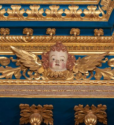 Zdjęcie nr 58: Ołtarz architektoniczny, trójosiowy, dwukondygnacyjny ze zwieńczeniem. Mensa prostopadłościenna, kamienna z drewnianym antepedium w formie leżącego prostokąta z postacią św. Augustyna ujętego wicią suchego akantu z przeplecioną, karbowaną wstążką i bukietami kwiatów. Przedstawienie otoczone profilowaną, ażurową ramą wypełnioną podobną wicią z akantu i kwiatów. Na mensie prostopadłościenne tabernakulum w formie kapliczki. Ściana frontowa z drzwiczkami w kształcie stojącego prostokąta dekorowanego krzyżem łacińskim ujętym wicią roślinną, zwieńczona trójkątnym przyczółkiem. Ścianka ujęta lizenami wypełnionymi wicią akantową podtrzymującymi pełne belkowanie obiegające bryłę, z mocno wysuniętym gzymsem wyłamanym w narożach. Całość zwieńczona czterospadowym dachem dekorowanym łuską. Na dachu baranek Boży leżący na księdze z siedmioma pieczęciami, przytrzymujący chorągiew, ukazany na tle chrystogramu otoczonego glorią promienistą. 
Nastawa na dwudzielnym cokole z półkolistymi bramkami ze zwieńczeniem utworzonym z ornamentu okuciowego ujmującego owalne pola. Osie pierwszej kondygnacji wydzielone kolumnami stojącymi na konsolach dekorowanych z frontu uskrzydlonymi główkami anielskimi powyżej liści akantu, na krawędziach cekinami, a po bokach wicią. Kolumny zostały przedzielone opaską w jednej trzeciej wysokości, dekorowane na całej wysokości wicią roślinną, główkami anielskimi w dolnej partii i imitacją kameryzacji na opaskach oraz w dwóch trzecich wysokości. Kolumny są ustawione na tle pilastrów dekorowanych wicią roślinną i zawieszonymi na niej chustkami. W polu centralnym kondygnacji jest nisza w kształcie stojącego prostokąta zamkniętego łukiem pełnym z postacią ukrzyżowanego Chrystusa na tle widoku Jerozolimy. W osiach bocznych mniejsze, ujęte pilastrami nisze o podobnym kształcie, których konchy wypełnione są muszlą, zwieńczone trójkątnym przyczółkiem przerwanym na cokół. W nich, na dekorowanych wicią i rozetami konsolach ustawiono figury: po lewej stronie św. Piotra, a po prawej św. Pawła. Kondygnacje ujmują ażurowe uszaki utworzone z ornamentu okuciowego, ulistnionych wolut i przewieszonej chustki. Kolumny podtrzymują pełne belkowanie wyniesione w łuk nad polem centralnym. Podłucze dekorowane rozetami, fryz głowami anielskimi i wicią, gzyms m.in. kostkowaniem i liśćmi akantu. Całość spięta kluczem z kartuszem z herbem kanoników regularnych od pokuty (marków). Na wyniesieniu belkowania posadowiono postaci aniołów trzymających narzędzia męki: anioł po lewej włócznię, a anioł po prawej gąbkę. Górna kondygnacja oparta została na schemacie aediculi – prostokątne pole ujęto kolumnami podtrzymującymi pełne belkowanie i trójkątny przyczółek przerwany na środku na cokół, na którym ustawiono rzeźbę  pelikana karmiącego młode własną krwią. Na krawędziach przyczółka dwie leżące postaci. Kondygnacja flankowana postaciami czterech ewangelistów ustawionymi na cokołach. Po lewej stronie św. Marek i św. Jan, po prawej św. Mateusz i św. Łukasz. Struktura polichromowana na kolor ciemnoniebieski; kolumny, profile, detale i ornamenty złocone i srebrzone.
