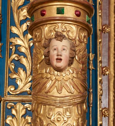 Zdjęcie nr 61: Ołtarz architektoniczny, trójosiowy, dwukondygnacyjny ze zwieńczeniem. Mensa prostopadłościenna, kamienna z drewnianym antepedium w formie leżącego prostokąta z postacią św. Augustyna ujętego wicią suchego akantu z przeplecioną, karbowaną wstążką i bukietami kwiatów. Przedstawienie otoczone profilowaną, ażurową ramą wypełnioną podobną wicią z akantu i kwiatów. Na mensie prostopadłościenne tabernakulum w formie kapliczki. Ściana frontowa z drzwiczkami w kształcie stojącego prostokąta dekorowanego krzyżem łacińskim ujętym wicią roślinną, zwieńczona trójkątnym przyczółkiem. Ścianka ujęta lizenami wypełnionymi wicią akantową podtrzymującymi pełne belkowanie obiegające bryłę, z mocno wysuniętym gzymsem wyłamanym w narożach. Całość zwieńczona czterospadowym dachem dekorowanym łuską. Na dachu baranek Boży leżący na księdze z siedmioma pieczęciami, przytrzymujący chorągiew, ukazany na tle chrystogramu otoczonego glorią promienistą. 
Nastawa na dwudzielnym cokole z półkolistymi bramkami ze zwieńczeniem utworzonym z ornamentu okuciowego ujmującego owalne pola. Osie pierwszej kondygnacji wydzielone kolumnami stojącymi na konsolach dekorowanych z frontu uskrzydlonymi główkami anielskimi powyżej liści akantu, na krawędziach cekinami, a po bokach wicią. Kolumny zostały przedzielone opaską w jednej trzeciej wysokości, dekorowane na całej wysokości wicią roślinną, główkami anielskimi w dolnej partii i imitacją kameryzacji na opaskach oraz w dwóch trzecich wysokości. Kolumny są ustawione na tle pilastrów dekorowanych wicią roślinną i zawieszonymi na niej chustkami. W polu centralnym kondygnacji jest nisza w kształcie stojącego prostokąta zamkniętego łukiem pełnym z postacią ukrzyżowanego Chrystusa na tle widoku Jerozolimy. W osiach bocznych mniejsze, ujęte pilastrami nisze o podobnym kształcie, których konchy wypełnione są muszlą, zwieńczone trójkątnym przyczółkiem przerwanym na cokół. W nich, na dekorowanych wicią i rozetami konsolach ustawiono figury: po lewej stronie św. Piotra, a po prawej św. Pawła. Kondygnacje ujmują ażurowe uszaki utworzone z ornamentu okuciowego, ulistnionych wolut i przewieszonej chustki. Kolumny podtrzymują pełne belkowanie wyniesione w łuk nad polem centralnym. Podłucze dekorowane rozetami, fryz głowami anielskimi i wicią, gzyms m.in. kostkowaniem i liśćmi akantu. Całość spięta kluczem z kartuszem z herbem kanoników regularnych od pokuty (marków). Na wyniesieniu belkowania posadowiono postaci aniołów trzymających narzędzia męki: anioł po lewej włócznię, a anioł po prawej gąbkę. Górna kondygnacja oparta została na schemacie aediculi – prostokątne pole ujęto kolumnami podtrzymującymi pełne belkowanie i trójkątny przyczółek przerwany na środku na cokół, na którym ustawiono rzeźbę  pelikana karmiącego młode własną krwią. Na krawędziach przyczółka dwie leżące postaci. Kondygnacja flankowana postaciami czterech ewangelistów ustawionymi na cokołach. Po lewej stronie św. Marek i św. Jan, po prawej św. Mateusz i św. Łukasz. Struktura polichromowana na kolor ciemnoniebieski; kolumny, profile, detale i ornamenty złocone i srebrzone.
