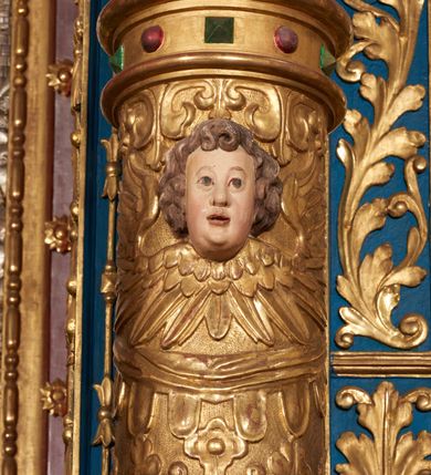 Zdjęcie nr 62: Ołtarz architektoniczny, trójosiowy, dwukondygnacyjny ze zwieńczeniem. Mensa prostopadłościenna, kamienna z drewnianym antepedium w formie leżącego prostokąta z postacią św. Augustyna ujętego wicią suchego akantu z przeplecioną, karbowaną wstążką i bukietami kwiatów. Przedstawienie otoczone profilowaną, ażurową ramą wypełnioną podobną wicią z akantu i kwiatów. Na mensie prostopadłościenne tabernakulum w formie kapliczki. Ściana frontowa z drzwiczkami w kształcie stojącego prostokąta dekorowanego krzyżem łacińskim ujętym wicią roślinną, zwieńczona trójkątnym przyczółkiem. Ścianka ujęta lizenami wypełnionymi wicią akantową podtrzymującymi pełne belkowanie obiegające bryłę, z mocno wysuniętym gzymsem wyłamanym w narożach. Całość zwieńczona czterospadowym dachem dekorowanym łuską. Na dachu baranek Boży leżący na księdze z siedmioma pieczęciami, przytrzymujący chorągiew, ukazany na tle chrystogramu otoczonego glorią promienistą. 
Nastawa na dwudzielnym cokole z półkolistymi bramkami ze zwieńczeniem utworzonym z ornamentu okuciowego ujmującego owalne pola. Osie pierwszej kondygnacji wydzielone kolumnami stojącymi na konsolach dekorowanych z frontu uskrzydlonymi główkami anielskimi powyżej liści akantu, na krawędziach cekinami, a po bokach wicią. Kolumny zostały przedzielone opaską w jednej trzeciej wysokości, dekorowane na całej wysokości wicią roślinną, główkami anielskimi w dolnej partii i imitacją kameryzacji na opaskach oraz w dwóch trzecich wysokości. Kolumny są ustawione na tle pilastrów dekorowanych wicią roślinną i zawieszonymi na niej chustkami. W polu centralnym kondygnacji jest nisza w kształcie stojącego prostokąta zamkniętego łukiem pełnym z postacią ukrzyżowanego Chrystusa na tle widoku Jerozolimy. W osiach bocznych mniejsze, ujęte pilastrami nisze o podobnym kształcie, których konchy wypełnione są muszlą, zwieńczone trójkątnym przyczółkiem przerwanym na cokół. W nich, na dekorowanych wicią i rozetami konsolach ustawiono figury: po lewej stronie św. Piotra, a po prawej św. Pawła. Kondygnacje ujmują ażurowe uszaki utworzone z ornamentu okuciowego, ulistnionych wolut i przewieszonej chustki. Kolumny podtrzymują pełne belkowanie wyniesione w łuk nad polem centralnym. Podłucze dekorowane rozetami, fryz głowami anielskimi i wicią, gzyms m.in. kostkowaniem i liśćmi akantu. Całość spięta kluczem z kartuszem z herbem kanoników regularnych od pokuty (marków). Na wyniesieniu belkowania posadowiono postaci aniołów trzymających narzędzia męki: anioł po lewej włócznię, a anioł po prawej gąbkę. Górna kondygnacja oparta została na schemacie aediculi – prostokątne pole ujęto kolumnami podtrzymującymi pełne belkowanie i trójkątny przyczółek przerwany na środku na cokół, na którym ustawiono rzeźbę  pelikana karmiącego młode własną krwią. Na krawędziach przyczółka dwie leżące postaci. Kondygnacja flankowana postaciami czterech ewangelistów ustawionymi na cokołach. Po lewej stronie św. Marek i św. Jan, po prawej św. Mateusz i św. Łukasz. Struktura polichromowana na kolor ciemnoniebieski; kolumny, profile, detale i ornamenty złocone i srebrzone.
