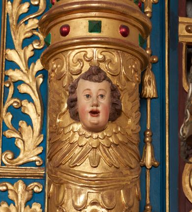 Zdjęcie nr 64: Ołtarz architektoniczny, trójosiowy, dwukondygnacyjny ze zwieńczeniem. Mensa prostopadłościenna, kamienna z drewnianym antepedium w formie leżącego prostokąta z postacią św. Augustyna ujętego wicią suchego akantu z przeplecioną, karbowaną wstążką i bukietami kwiatów. Przedstawienie otoczone profilowaną, ażurową ramą wypełnioną podobną wicią z akantu i kwiatów. Na mensie prostopadłościenne tabernakulum w formie kapliczki. Ściana frontowa z drzwiczkami w kształcie stojącego prostokąta dekorowanego krzyżem łacińskim ujętym wicią roślinną, zwieńczona trójkątnym przyczółkiem. Ścianka ujęta lizenami wypełnionymi wicią akantową podtrzymującymi pełne belkowanie obiegające bryłę, z mocno wysuniętym gzymsem wyłamanym w narożach. Całość zwieńczona czterospadowym dachem dekorowanym łuską. Na dachu baranek Boży leżący na księdze z siedmioma pieczęciami, przytrzymujący chorągiew, ukazany na tle chrystogramu otoczonego glorią promienistą. 
Nastawa na dwudzielnym cokole z półkolistymi bramkami ze zwieńczeniem utworzonym z ornamentu okuciowego ujmującego owalne pola. Osie pierwszej kondygnacji wydzielone kolumnami stojącymi na konsolach dekorowanych z frontu uskrzydlonymi główkami anielskimi powyżej liści akantu, na krawędziach cekinami, a po bokach wicią. Kolumny zostały przedzielone opaską w jednej trzeciej wysokości, dekorowane na całej wysokości wicią roślinną, główkami anielskimi w dolnej partii i imitacją kameryzacji na opaskach oraz w dwóch trzecich wysokości. Kolumny są ustawione na tle pilastrów dekorowanych wicią roślinną i zawieszonymi na niej chustkami. W polu centralnym kondygnacji jest nisza w kształcie stojącego prostokąta zamkniętego łukiem pełnym z postacią ukrzyżowanego Chrystusa na tle widoku Jerozolimy. W osiach bocznych mniejsze, ujęte pilastrami nisze o podobnym kształcie, których konchy wypełnione są muszlą, zwieńczone trójkątnym przyczółkiem przerwanym na cokół. W nich, na dekorowanych wicią i rozetami konsolach ustawiono figury: po lewej stronie św. Piotra, a po prawej św. Pawła. Kondygnacje ujmują ażurowe uszaki utworzone z ornamentu okuciowego, ulistnionych wolut i przewieszonej chustki. Kolumny podtrzymują pełne belkowanie wyniesione w łuk nad polem centralnym. Podłucze dekorowane rozetami, fryz głowami anielskimi i wicią, gzyms m.in. kostkowaniem i liśćmi akantu. Całość spięta kluczem z kartuszem z herbem kanoników regularnych od pokuty (marków). Na wyniesieniu belkowania posadowiono postaci aniołów trzymających narzędzia męki: anioł po lewej włócznię, a anioł po prawej gąbkę. Górna kondygnacja oparta została na schemacie aediculi – prostokątne pole ujęto kolumnami podtrzymującymi pełne belkowanie i trójkątny przyczółek przerwany na środku na cokół, na którym ustawiono rzeźbę  pelikana karmiącego młode własną krwią. Na krawędziach przyczółka dwie leżące postaci. Kondygnacja flankowana postaciami czterech ewangelistów ustawionymi na cokołach. Po lewej stronie św. Marek i św. Jan, po prawej św. Mateusz i św. Łukasz. Struktura polichromowana na kolor ciemnoniebieski; kolumny, profile, detale i ornamenty złocone i srebrzone.
