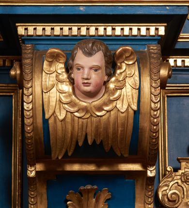 Zdjęcie nr 65: Ołtarz architektoniczny, trójosiowy, dwukondygnacyjny ze zwieńczeniem. Mensa prostopadłościenna, kamienna z drewnianym antepedium w formie leżącego prostokąta z postacią św. Augustyna ujętego wicią suchego akantu z przeplecioną, karbowaną wstążką i bukietami kwiatów. Przedstawienie otoczone profilowaną, ażurową ramą wypełnioną podobną wicią z akantu i kwiatów. Na mensie prostopadłościenne tabernakulum w formie kapliczki. Ściana frontowa z drzwiczkami w kształcie stojącego prostokąta dekorowanego krzyżem łacińskim ujętym wicią roślinną, zwieńczona trójkątnym przyczółkiem. Ścianka ujęta lizenami wypełnionymi wicią akantową podtrzymującymi pełne belkowanie obiegające bryłę, z mocno wysuniętym gzymsem wyłamanym w narożach. Całość zwieńczona czterospadowym dachem dekorowanym łuską. Na dachu baranek Boży leżący na księdze z siedmioma pieczęciami, przytrzymujący chorągiew, ukazany na tle chrystogramu otoczonego glorią promienistą. 
Nastawa na dwudzielnym cokole z półkolistymi bramkami ze zwieńczeniem utworzonym z ornamentu okuciowego ujmującego owalne pola. Osie pierwszej kondygnacji wydzielone kolumnami stojącymi na konsolach dekorowanych z frontu uskrzydlonymi główkami anielskimi powyżej liści akantu, na krawędziach cekinami, a po bokach wicią. Kolumny zostały przedzielone opaską w jednej trzeciej wysokości, dekorowane na całej wysokości wicią roślinną, główkami anielskimi w dolnej partii i imitacją kameryzacji na opaskach oraz w dwóch trzecich wysokości. Kolumny są ustawione na tle pilastrów dekorowanych wicią roślinną i zawieszonymi na niej chustkami. W polu centralnym kondygnacji jest nisza w kształcie stojącego prostokąta zamkniętego łukiem pełnym z postacią ukrzyżowanego Chrystusa na tle widoku Jerozolimy. W osiach bocznych mniejsze, ujęte pilastrami nisze o podobnym kształcie, których konchy wypełnione są muszlą, zwieńczone trójkątnym przyczółkiem przerwanym na cokół. W nich, na dekorowanych wicią i rozetami konsolach ustawiono figury: po lewej stronie św. Piotra, a po prawej św. Pawła. Kondygnacje ujmują ażurowe uszaki utworzone z ornamentu okuciowego, ulistnionych wolut i przewieszonej chustki. Kolumny podtrzymują pełne belkowanie wyniesione w łuk nad polem centralnym. Podłucze dekorowane rozetami, fryz głowami anielskimi i wicią, gzyms m.in. kostkowaniem i liśćmi akantu. Całość spięta kluczem z kartuszem z herbem kanoników regularnych od pokuty (marków). Na wyniesieniu belkowania posadowiono postaci aniołów trzymających narzędzia męki: anioł po lewej włócznię, a anioł po prawej gąbkę. Górna kondygnacja oparta została na schemacie aediculi – prostokątne pole ujęto kolumnami podtrzymującymi pełne belkowanie i trójkątny przyczółek przerwany na środku na cokół, na którym ustawiono rzeźbę  pelikana karmiącego młode własną krwią. Na krawędziach przyczółka dwie leżące postaci. Kondygnacja flankowana postaciami czterech ewangelistów ustawionymi na cokołach. Po lewej stronie św. Marek i św. Jan, po prawej św. Mateusz i św. Łukasz. Struktura polichromowana na kolor ciemnoniebieski; kolumny, profile, detale i ornamenty złocone i srebrzone.
