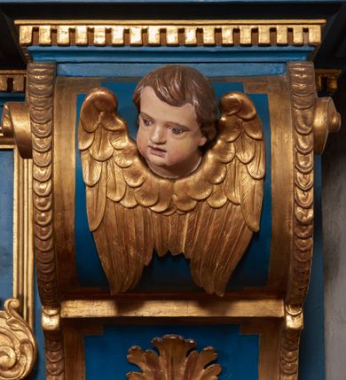 Zdjęcie nr 67: Ołtarz architektoniczny, trójosiowy, dwukondygnacyjny ze zwieńczeniem. Mensa prostopadłościenna, kamienna z drewnianym antepedium w formie leżącego prostokąta z postacią św. Augustyna ujętego wicią suchego akantu z przeplecioną, karbowaną wstążką i bukietami kwiatów. Przedstawienie otoczone profilowaną, ażurową ramą wypełnioną podobną wicią z akantu i kwiatów. Na mensie prostopadłościenne tabernakulum w formie kapliczki. Ściana frontowa z drzwiczkami w kształcie stojącego prostokąta dekorowanego krzyżem łacińskim ujętym wicią roślinną, zwieńczona trójkątnym przyczółkiem. Ścianka ujęta lizenami wypełnionymi wicią akantową podtrzymującymi pełne belkowanie obiegające bryłę, z mocno wysuniętym gzymsem wyłamanym w narożach. Całość zwieńczona czterospadowym dachem dekorowanym łuską. Na dachu baranek Boży leżący na księdze z siedmioma pieczęciami, przytrzymujący chorągiew, ukazany na tle chrystogramu otoczonego glorią promienistą. 
Nastawa na dwudzielnym cokole z półkolistymi bramkami ze zwieńczeniem utworzonym z ornamentu okuciowego ujmującego owalne pola. Osie pierwszej kondygnacji wydzielone kolumnami stojącymi na konsolach dekorowanych z frontu uskrzydlonymi główkami anielskimi powyżej liści akantu, na krawędziach cekinami, a po bokach wicią. Kolumny zostały przedzielone opaską w jednej trzeciej wysokości, dekorowane na całej wysokości wicią roślinną, główkami anielskimi w dolnej partii i imitacją kameryzacji na opaskach oraz w dwóch trzecich wysokości. Kolumny są ustawione na tle pilastrów dekorowanych wicią roślinną i zawieszonymi na niej chustkami. W polu centralnym kondygnacji jest nisza w kształcie stojącego prostokąta zamkniętego łukiem pełnym z postacią ukrzyżowanego Chrystusa na tle widoku Jerozolimy. W osiach bocznych mniejsze, ujęte pilastrami nisze o podobnym kształcie, których konchy wypełnione są muszlą, zwieńczone trójkątnym przyczółkiem przerwanym na cokół. W nich, na dekorowanych wicią i rozetami konsolach ustawiono figury: po lewej stronie św. Piotra, a po prawej św. Pawła. Kondygnacje ujmują ażurowe uszaki utworzone z ornamentu okuciowego, ulistnionych wolut i przewieszonej chustki. Kolumny podtrzymują pełne belkowanie wyniesione w łuk nad polem centralnym. Podłucze dekorowane rozetami, fryz głowami anielskimi i wicią, gzyms m.in. kostkowaniem i liśćmi akantu. Całość spięta kluczem z kartuszem z herbem kanoników regularnych od pokuty (marków). Na wyniesieniu belkowania posadowiono postaci aniołów trzymających narzędzia męki: anioł po lewej włócznię, a anioł po prawej gąbkę. Górna kondygnacja oparta została na schemacie aediculi – prostokątne pole ujęto kolumnami podtrzymującymi pełne belkowanie i trójkątny przyczółek przerwany na środku na cokół, na którym ustawiono rzeźbę  pelikana karmiącego młode własną krwią. Na krawędziach przyczółka dwie leżące postaci. Kondygnacja flankowana postaciami czterech ewangelistów ustawionymi na cokołach. Po lewej stronie św. Marek i św. Jan, po prawej św. Mateusz i św. Łukasz. Struktura polichromowana na kolor ciemnoniebieski; kolumny, profile, detale i ornamenty złocone i srebrzone.
