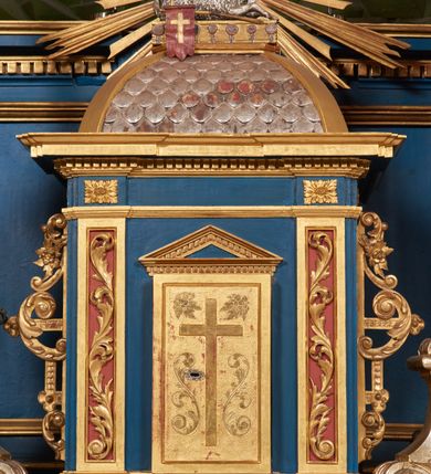 Zdjęcie nr 68: Ołtarz architektoniczny, trójosiowy, dwukondygnacyjny ze zwieńczeniem. Mensa prostopadłościenna, kamienna z drewnianym antepedium w formie leżącego prostokąta z postacią św. Augustyna ujętego wicią suchego akantu z przeplecioną, karbowaną wstążką i bukietami kwiatów. Przedstawienie otoczone profilowaną, ażurową ramą wypełnioną podobną wicią z akantu i kwiatów. Na mensie prostopadłościenne tabernakulum w formie kapliczki. Ściana frontowa z drzwiczkami w kształcie stojącego prostokąta dekorowanego krzyżem łacińskim ujętym wicią roślinną, zwieńczona trójkątnym przyczółkiem. Ścianka ujęta lizenami wypełnionymi wicią akantową podtrzymującymi pełne belkowanie obiegające bryłę, z mocno wysuniętym gzymsem wyłamanym w narożach. Całość zwieńczona czterospadowym dachem dekorowanym łuską. Na dachu baranek Boży leżący na księdze z siedmioma pieczęciami, przytrzymujący chorągiew, ukazany na tle chrystogramu otoczonego glorią promienistą. 
Nastawa na dwudzielnym cokole z półkolistymi bramkami ze zwieńczeniem utworzonym z ornamentu okuciowego ujmującego owalne pola. Osie pierwszej kondygnacji wydzielone kolumnami stojącymi na konsolach dekorowanych z frontu uskrzydlonymi główkami anielskimi powyżej liści akantu, na krawędziach cekinami, a po bokach wicią. Kolumny zostały przedzielone opaską w jednej trzeciej wysokości, dekorowane na całej wysokości wicią roślinną, główkami anielskimi w dolnej partii i imitacją kameryzacji na opaskach oraz w dwóch trzecich wysokości. Kolumny są ustawione na tle pilastrów dekorowanych wicią roślinną i zawieszonymi na niej chustkami. W polu centralnym kondygnacji jest nisza w kształcie stojącego prostokąta zamkniętego łukiem pełnym z postacią ukrzyżowanego Chrystusa na tle widoku Jerozolimy. W osiach bocznych mniejsze, ujęte pilastrami nisze o podobnym kształcie, których konchy wypełnione są muszlą, zwieńczone trójkątnym przyczółkiem przerwanym na cokół. W nich, na dekorowanych wicią i rozetami konsolach ustawiono figury: po lewej stronie św. Piotra, a po prawej św. Pawła. Kondygnacje ujmują ażurowe uszaki utworzone z ornamentu okuciowego, ulistnionych wolut i przewieszonej chustki. Kolumny podtrzymują pełne belkowanie wyniesione w łuk nad polem centralnym. Podłucze dekorowane rozetami, fryz głowami anielskimi i wicią, gzyms m.in. kostkowaniem i liśćmi akantu. Całość spięta kluczem z kartuszem z herbem kanoników regularnych od pokuty (marków). Na wyniesieniu belkowania posadowiono postaci aniołów trzymających narzędzia męki: anioł po lewej włócznię, a anioł po prawej gąbkę. Górna kondygnacja oparta została na schemacie aediculi – prostokątne pole ujęto kolumnami podtrzymującymi pełne belkowanie i trójkątny przyczółek przerwany na środku na cokół, na którym ustawiono rzeźbę  pelikana karmiącego młode własną krwią. Na krawędziach przyczółka dwie leżące postaci. Kondygnacja flankowana postaciami czterech ewangelistów ustawionymi na cokołach. Po lewej stronie św. Marek i św. Jan, po prawej św. Mateusz i św. Łukasz. Struktura polichromowana na kolor ciemnoniebieski; kolumny, profile, detale i ornamenty złocone i srebrzone.
