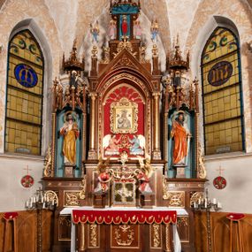 Zdjęcie nr 1: Ołtarz jednokondygnacyjny na wysokim, schodkowym cokole, trójosiowy, z wysuniętą mensą ołtarzową. Płyciny cokołu zdobione dekoracją w formie ostrołukowych maswerków i rozet w kwadratowej ramie. Antepedium flankowane parą kolumn ustawionych na wysokich cokołach i kanelowanych, skręconych trzonach z kompozytowymi kapitelami. W polu dwie prostokątne płyciny i kwadratowa pośrodku ze stylizowaną wicią roślinną i małą uskrzydloną główką aniołka. Tabernakulum proste, w kształcie prostopadłościennej skrzynki, o złotych drzwiczkach z wytłaczaną formą równoramiennego krzyża i wypukłą srebrną rybą oraz koszem z chlebem. Po obu stronach, na niewysokich postumentach dwa klęczące anioły z wysokimi skrzydłami, w biało różowych szatach z fioletowym podbiciem (skrzydła stylizowane na husarskie). Anioł po lewej z kadzielnicą, a anioł po prawej z kielichem.
Nastawa ołtarzowa o trzech oddzielnych niszach, nakrytych gotycyzującymi baldachimami z pinaklami, ozdobionymi żabkami. Oś środkowa w formie niszy zamkniętej ostrołukowo z wimpergą wspartą na smukłych, złoconych kolumienkach o kapitelach kompozytowych. Wimperga ze złoconymi, profilowanymi płycinami, zwieńczona rzeźbionymi liśćmi akantu i wolutami. Na przedłużeniu kolumn postumenty z figurami aniołów w biało niebieskich szatach, ze złotymi, wydłużonymi skrzydłami. Na osi na postumencie, pod gotycyzującym baldachimem figura świętego biskupa w czerwonej szacie z krzyżem w dłoni pomiędzy dwoma aniołami w białych i różowych szatach. W niszy, na czerwonym tle obraz Matki Boskiej Nieustającej Pomocy w prostej ramie z dekoracją w formie wici roślinnej. Poniżej dwa płaskorzeźbione anioły trzymające ażurowy monogram maryjny. Anioły o pozłacanych skrzydłach, na chmurach, w różowej i niebieskiej szacie. Osie boczne w formie aediculi z gotycyzującym baldachimem. W niszach figury, po lewej św. Piotra, a po prawej św. Pawła. Aedicule ujęte są smukłymi, skręconymi kolumnami z kapitelami wolutowymi oraz roślinnym uszakiem z perełkowaniem. Nad nimi imposty, na których rzeźby osłaniane baldachimami, po lewej świętego w habicie jezuity, a po prawej św. Jana Kantego. Drewno bejcowane na ciemny brąz, z nakładanymi elementami dekoracyjnymi złoconymi. 