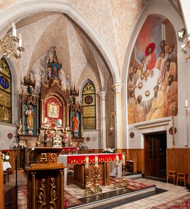 Zdjęcie nr 13: Ołtarz jednokondygnacyjny na wysokim, schodkowym cokole, trójosiowy, z wysuniętą mensą ołtarzową. Płyciny cokołu zdobione dekoracją w formie ostrołukowych maswerków i rozet w kwadratowej ramie. Antepedium flankowane parą kolumn ustawionych na wysokich cokołach i kanelowanych, skręconych trzonach z kompozytowymi kapitelami. W polu dwie prostokątne płyciny i kwadratowa pośrodku ze stylizowaną wicią roślinną i małą uskrzydloną główką aniołka. Tabernakulum proste, w kształcie prostopadłościennej skrzynki, o złotych drzwiczkach z wytłaczaną formą równoramiennego krzyża i wypukłą srebrną rybą oraz koszem z chlebem. Po obu stronach, na niewysokich postumentach dwa klęczące anioły z wysokimi skrzydłami, w biało różowych szatach z fioletowym podbiciem (skrzydła stylizowane na husarskie). Anioł po lewej z kadzielnicą, a anioł po prawej z kielichem.
Nastawa ołtarzowa o trzech oddzielnych niszach, nakrytych gotycyzującymi baldachimami z pinaklami, ozdobionymi żabkami. Oś środkowa w formie niszy zamkniętej ostrołukowo z wimpergą wspartą na smukłych, złoconych kolumienkach o kapitelach kompozytowych. Wimperga ze złoconymi, profilowanymi płycinami, zwieńczona rzeźbionymi liśćmi akantu i wolutami. Na przedłużeniu kolumn postumenty z figurami aniołów w biało niebieskich szatach, ze złotymi, wydłużonymi skrzydłami. Na osi na postumencie, pod gotycyzującym baldachimem figura świętego biskupa w czerwonej szacie z krzyżem w dłoni pomiędzy dwoma aniołami w białych i różowych szatach. W niszy, na czerwonym tle obraz Matki Boskiej Nieustającej Pomocy w prostej ramie z dekoracją w formie wici roślinnej. Poniżej dwa płaskorzeźbione anioły trzymające ażurowy monogram maryjny. Anioły o pozłacanych skrzydłach, na chmurach, w różowej i niebieskiej szacie. Osie boczne w formie aediculi z gotycyzującym baldachimem. W niszach figury, po lewej św. Piotra, a po prawej św. Pawła. Aedicule ujęte są smukłymi, skręconymi kolumnami z kapitelami wolutowymi oraz roślinnym uszakiem z perełkowaniem. Nad nimi imposty, na których rzeźby osłaniane baldachimami, po lewej świętego w habicie jezuity, a po prawej św. Jana Kantego. Drewno bejcowane na ciemny brąz, z nakładanymi elementami dekoracyjnymi złoconymi. 