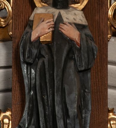 Zdjęcie nr 4: Ołtarz jednokondygnacyjny na wysokim, schodkowym cokole, trójosiowy, z wysuniętą mensą ołtarzową. Płyciny cokołu zdobione dekoracją w formie ostrołukowych maswerków i rozet w kwadratowej ramie. Antepedium flankowane parą kolumn ustawionych na wysokich cokołach i kanelowanych, skręconych trzonach z kompozytowymi kapitelami. W polu dwie prostokątne płyciny i kwadratowa pośrodku ze stylizowaną wicią roślinną i małą uskrzydloną główką aniołka. Tabernakulum proste, w kształcie prostopadłościennej skrzynki, o złotych drzwiczkach z wytłaczaną formą równoramiennego krzyża i wypukłą srebrną rybą oraz koszem z chlebem. Po obu stronach, na niewysokich postumentach dwa klęczące anioły z wysokimi skrzydłami, w biało różowych szatach z fioletowym podbiciem (skrzydła stylizowane na husarskie). Anioł po lewej z kadzielnicą, a anioł po prawej z kielichem.
Nastawa ołtarzowa o trzech oddzielnych niszach, nakrytych gotycyzującymi baldachimami z pinaklami, ozdobionymi żabkami. Oś środkowa w formie niszy zamkniętej ostrołukowo z wimpergą wspartą na smukłych, złoconych kolumienkach o kapitelach kompozytowych. Wimperga ze złoconymi, profilowanymi płycinami, zwieńczona rzeźbionymi liśćmi akantu i wolutami. Na przedłużeniu kolumn postumenty z figurami aniołów w biało niebieskich szatach, ze złotymi, wydłużonymi skrzydłami. Na osi na postumencie, pod gotycyzującym baldachimem figura świętego biskupa w czerwonej szacie z krzyżem w dłoni pomiędzy dwoma aniołami w białych i różowych szatach. W niszy, na czerwonym tle obraz Matki Boskiej Nieustającej Pomocy w prostej ramie z dekoracją w formie wici roślinnej. Poniżej dwa płaskorzeźbione anioły trzymające ażurowy monogram maryjny. Anioły o pozłacanych skrzydłach, na chmurach, w różowej i niebieskiej szacie. Osie boczne w formie aediculi z gotycyzującym baldachimem. W niszach figury, po lewej św. Piotra, a po prawej św. Pawła. Aedicule ujęte są smukłymi, skręconymi kolumnami z kapitelami wolutowymi oraz roślinnym uszakiem z perełkowaniem. Nad nimi imposty, na których rzeźby osłaniane baldachimami, po lewej świętego w habicie jezuity, a po prawej św. Jana Kantego. Drewno bejcowane na ciemny brąz, z nakładanymi elementami dekoracyjnymi złoconymi. 