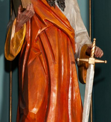 Zdjęcie nr 18: Ołtarz jednokondygnacyjny na wysokim, schodkowym cokole, trójosiowy, z wysuniętą mensą ołtarzową. Płyciny cokołu zdobione dekoracją w formie ostrołukowych maswerków i rozet w kwadratowej ramie. Antepedium flankowane parą kolumn ustawionych na wysokich cokołach i kanelowanych, skręconych trzonach z kompozytowymi kapitelami. W polu dwie prostokątne płyciny i kwadratowa pośrodku ze stylizowaną wicią roślinną i małą uskrzydloną główką aniołka. Tabernakulum proste, w kształcie prostopadłościennej skrzynki, o złotych drzwiczkach z wytłaczaną formą równoramiennego krzyża i wypukłą srebrną rybą oraz koszem z chlebem. Po obu stronach, na niewysokich postumentach dwa klęczące anioły z wysokimi skrzydłami, w biało różowych szatach z fioletowym podbiciem (skrzydła stylizowane na husarskie). Anioł po lewej z kadzielnicą, a anioł po prawej z kielichem.
Nastawa ołtarzowa o trzech oddzielnych niszach, nakrytych gotycyzującymi baldachimami z pinaklami, ozdobionymi żabkami. Oś środkowa w formie niszy zamkniętej ostrołukowo z wimpergą wspartą na smukłych, złoconych kolumienkach o kapitelach kompozytowych. Wimperga ze złoconymi, profilowanymi płycinami, zwieńczona rzeźbionymi liśćmi akantu i wolutami. Na przedłużeniu kolumn postumenty z figurami aniołów w biało niebieskich szatach, ze złotymi, wydłużonymi skrzydłami. Na osi na postumencie, pod gotycyzującym baldachimem figura świętego biskupa w czerwonej szacie z krzyżem w dłoni pomiędzy dwoma aniołami w białych i różowych szatach. W niszy, na czerwonym tle obraz Matki Boskiej Nieustającej Pomocy w prostej ramie z dekoracją w formie wici roślinnej. Poniżej dwa płaskorzeźbione anioły trzymające ażurowy monogram maryjny. Anioły o pozłacanych skrzydłach, na chmurach, w różowej i niebieskiej szacie. Osie boczne w formie aediculi z gotycyzującym baldachimem. W niszach figury, po lewej św. Piotra, a po prawej św. Pawła. Aedicule ujęte są smukłymi, skręconymi kolumnami z kapitelami wolutowymi oraz roślinnym uszakiem z perełkowaniem. Nad nimi imposty, na których rzeźby osłaniane baldachimami, po lewej świętego w habicie jezuity, a po prawej św. Jana Kantego. Drewno bejcowane na ciemny brąz, z nakładanymi elementami dekoracyjnymi złoconymi. 