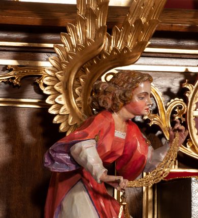 Zdjęcie nr 23: Ołtarz jednokondygnacyjny na wysokim, schodkowym cokole, trójosiowy, z wysuniętą mensą ołtarzową. Płyciny cokołu zdobione dekoracją w formie ostrołukowych maswerków i rozet w kwadratowej ramie. Antepedium flankowane parą kolumn ustawionych na wysokich cokołach i kanelowanych, skręconych trzonach z kompozytowymi kapitelami. W polu dwie prostokątne płyciny i kwadratowa pośrodku ze stylizowaną wicią roślinną i małą uskrzydloną główką aniołka. Tabernakulum proste, w kształcie prostopadłościennej skrzynki, o złotych drzwiczkach z wytłaczaną formą równoramiennego krzyża i wypukłą srebrną rybą oraz koszem z chlebem. Po obu stronach, na niewysokich postumentach dwa klęczące anioły z wysokimi skrzydłami, w biało różowych szatach z fioletowym podbiciem (skrzydła stylizowane na husarskie). Anioł po lewej z kadzielnicą, a anioł po prawej z kielichem.
Nastawa ołtarzowa o trzech oddzielnych niszach, nakrytych gotycyzującymi baldachimami z pinaklami, ozdobionymi żabkami. Oś środkowa w formie niszy zamkniętej ostrołukowo z wimpergą wspartą na smukłych, złoconych kolumienkach o kapitelach kompozytowych. Wimperga ze złoconymi, profilowanymi płycinami, zwieńczona rzeźbionymi liśćmi akantu i wolutami. Na przedłużeniu kolumn postumenty z figurami aniołów w biało niebieskich szatach, ze złotymi, wydłużonymi skrzydłami. Na osi na postumencie, pod gotycyzującym baldachimem figura świętego biskupa w czerwonej szacie z krzyżem w dłoni pomiędzy dwoma aniołami w białych i różowych szatach. W niszy, na czerwonym tle obraz Matki Boskiej Nieustającej Pomocy w prostej ramie z dekoracją w formie wici roślinnej. Poniżej dwa płaskorzeźbione anioły trzymające ażurowy monogram maryjny. Anioły o pozłacanych skrzydłach, na chmurach, w różowej i niebieskiej szacie. Osie boczne w formie aediculi z gotycyzującym baldachimem. W niszach figury, po lewej św. Piotra, a po prawej św. Pawła. Aedicule ujęte są smukłymi, skręconymi kolumnami z kapitelami wolutowymi oraz roślinnym uszakiem z perełkowaniem. Nad nimi imposty, na których rzeźby osłaniane baldachimami, po lewej świętego w habicie jezuity, a po prawej św. Jana Kantego. Drewno bejcowane na ciemny brąz, z nakładanymi elementami dekoracyjnymi złoconymi. 