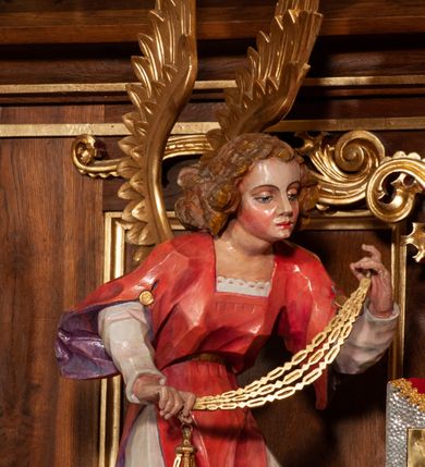 Zdjęcie nr 25: Ołtarz jednokondygnacyjny na wysokim, schodkowym cokole, trójosiowy, z wysuniętą mensą ołtarzową. Płyciny cokołu zdobione dekoracją w formie ostrołukowych maswerków i rozet w kwadratowej ramie. Antepedium flankowane parą kolumn ustawionych na wysokich cokołach i kanelowanych, skręconych trzonach z kompozytowymi kapitelami. W polu dwie prostokątne płyciny i kwadratowa pośrodku ze stylizowaną wicią roślinną i małą uskrzydloną główką aniołka. Tabernakulum proste, w kształcie prostopadłościennej skrzynki, o złotych drzwiczkach z wytłaczaną formą równoramiennego krzyża i wypukłą srebrną rybą oraz koszem z chlebem. Po obu stronach, na niewysokich postumentach dwa klęczące anioły z wysokimi skrzydłami, w biało różowych szatach z fioletowym podbiciem (skrzydła stylizowane na husarskie). Anioł po lewej z kadzielnicą, a anioł po prawej z kielichem.
Nastawa ołtarzowa o trzech oddzielnych niszach, nakrytych gotycyzującymi baldachimami z pinaklami, ozdobionymi żabkami. Oś środkowa w formie niszy zamkniętej ostrołukowo z wimpergą wspartą na smukłych, złoconych kolumienkach o kapitelach kompozytowych. Wimperga ze złoconymi, profilowanymi płycinami, zwieńczona rzeźbionymi liśćmi akantu i wolutami. Na przedłużeniu kolumn postumenty z figurami aniołów w biało niebieskich szatach, ze złotymi, wydłużonymi skrzydłami. Na osi na postumencie, pod gotycyzującym baldachimem figura świętego biskupa w czerwonej szacie z krzyżem w dłoni pomiędzy dwoma aniołami w białych i różowych szatach. W niszy, na czerwonym tle obraz Matki Boskiej Nieustającej Pomocy w prostej ramie z dekoracją w formie wici roślinnej. Poniżej dwa płaskorzeźbione anioły trzymające ażurowy monogram maryjny. Anioły o pozłacanych skrzydłach, na chmurach, w różowej i niebieskiej szacie. Osie boczne w formie aediculi z gotycyzującym baldachimem. W niszach figury, po lewej św. Piotra, a po prawej św. Pawła. Aedicule ujęte są smukłymi, skręconymi kolumnami z kapitelami wolutowymi oraz roślinnym uszakiem z perełkowaniem. Nad nimi imposty, na których rzeźby osłaniane baldachimami, po lewej świętego w habicie jezuity, a po prawej św. Jana Kantego. Drewno bejcowane na ciemny brąz, z nakładanymi elementami dekoracyjnymi złoconymi. 