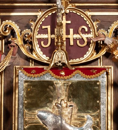 Zdjęcie nr 29: Ołtarz jednokondygnacyjny na wysokim, schodkowym cokole, trójosiowy, z wysuniętą mensą ołtarzową. Płyciny cokołu zdobione dekoracją w formie ostrołukowych maswerków i rozet w kwadratowej ramie. Antepedium flankowane parą kolumn ustawionych na wysokich cokołach i kanelowanych, skręconych trzonach z kompozytowymi kapitelami. W polu dwie prostokątne płyciny i kwadratowa pośrodku ze stylizowaną wicią roślinną i małą uskrzydloną główką aniołka. Tabernakulum proste, w kształcie prostopadłościennej skrzynki, o złotych drzwiczkach z wytłaczaną formą równoramiennego krzyża i wypukłą srebrną rybą oraz koszem z chlebem. Po obu stronach, na niewysokich postumentach dwa klęczące anioły z wysokimi skrzydłami, w biało różowych szatach z fioletowym podbiciem (skrzydła stylizowane na husarskie). Anioł po lewej z kadzielnicą, a anioł po prawej z kielichem.
Nastawa ołtarzowa o trzech oddzielnych niszach, nakrytych gotycyzującymi baldachimami z pinaklami, ozdobionymi żabkami. Oś środkowa w formie niszy zamkniętej ostrołukowo z wimpergą wspartą na smukłych, złoconych kolumienkach o kapitelach kompozytowych. Wimperga ze złoconymi, profilowanymi płycinami, zwieńczona rzeźbionymi liśćmi akantu i wolutami. Na przedłużeniu kolumn postumenty z figurami aniołów w biało niebieskich szatach, ze złotymi, wydłużonymi skrzydłami. Na osi na postumencie, pod gotycyzującym baldachimem figura świętego biskupa w czerwonej szacie z krzyżem w dłoni pomiędzy dwoma aniołami w białych i różowych szatach. W niszy, na czerwonym tle obraz Matki Boskiej Nieustającej Pomocy w prostej ramie z dekoracją w formie wici roślinnej. Poniżej dwa płaskorzeźbione anioły trzymające ażurowy monogram maryjny. Anioły o pozłacanych skrzydłach, na chmurach, w różowej i niebieskiej szacie. Osie boczne w formie aediculi z gotycyzującym baldachimem. W niszach figury, po lewej św. Piotra, a po prawej św. Pawła. Aedicule ujęte są smukłymi, skręconymi kolumnami z kapitelami wolutowymi oraz roślinnym uszakiem z perełkowaniem. Nad nimi imposty, na których rzeźby osłaniane baldachimami, po lewej świętego w habicie jezuity, a po prawej św. Jana Kantego. Drewno bejcowane na ciemny brąz, z nakładanymi elementami dekoracyjnymi złoconymi. 