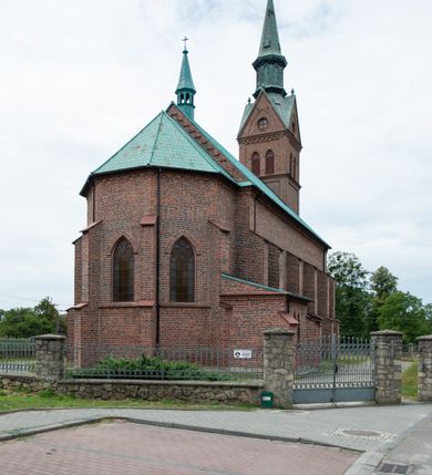 Zdjęcie nr 24: Kościół ceglany, na planie prostokąta z węższym i niższym prezbiterium z zakrystią od północy i wieżą od zachodu. Kościół orientowany, jednonawowy, czteroprzęsłowy z węższym, jednoprzęsłowym prezbiterium zamkniętym trójbocznie, z kruchtą w przyziemiu wieży. Nawa artykułowana półfilarami o ściętych narożach, przechodzącymi w zamknięte łukiem ostrym gurty krzyżowo-żebrowego sklepienia. W nawie i prezbiterium okna prostokątne zamknięte łukiem ostrym – pięć w prezbiterium, po trzy z każdej strony nawy. Węższe okna w przęśle chóru, kolejne w fasadzie. Główne wejście od wschodu, drugie od zachodu. Chór muzyczny w czwartym przęśle nawy, wsparty na wielobocznych filarach, podtrzymujących ostrołukowe arkady, z parapetem ozdobionym blendami. Ściany w dolnej partii pokryte drewnianą boazerią, wyżej malowane na kremowo, w partiach sklepienia polichromia podkreślająca elementy konstrukcji fragmentami stylizowanej wici i dekoracji floralnej; na belce tęczowej anioły niosące plakiety z symbolami świętych sakramentów. Fasada trójosiowa, z ryzalitem szerokości wieży oszkarpowanym na narożach. Podziały poziome przeprowadzone przy pomocy gzymsów. Na osi ostrołukowe wejście, powyżej wypełniony maswerkiem okulus. Następna kondygnacja jest częścią czworobocznej wieży, wypełniono ją dużym oknem w kształcę stojącego prostokąta zamkniętego łukiem ostrym.  Boczne osie z małymi oknami powtarzającymi kształt pozostałych, zamknięte trójkątnym przyczółkiem przerwanym na wieżę. Najwyższa kondygnacja wieży przepruta z każdej strony parą okien w kształcie stojących prostokątów umieszczonych w ostrołukowych niszach. Wieńczący ją gzyms dekorowany zygzakiem, powyżej trójkątne szczyty z ostrołukową blendą z okulusem w centrum. Elewacje boczne i prezbiterium oszkarpowane, przeprute oknami.  Hełm wieży w formie latarni zakończonej stożkiem z kupą i krzyżem, nawa przekryta dachem dwuspadowym, prezbiterium wielobocznym, zakrystia i wejście od zachodu pulpitowymi. 


Do najciekawszych elementów wyposażenia należą zespół neogotyckich ołtarzy wraz z amboną oraz kolekcja dziewiętnastowiecznych feretronów. W otoczeniu kościoła znajduje się kamienna figura św. Jana Nepomucena z 1788 roku. 
