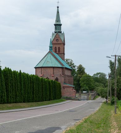 Zdjęcie nr 35: Kościół ceglany, na planie prostokąta z węższym i niższym prezbiterium z zakrystią od północy i wieżą od zachodu. Kościół orientowany, jednonawowy, czteroprzęsłowy z węższym, jednoprzęsłowym prezbiterium zamkniętym trójbocznie, z kruchtą w przyziemiu wieży. Nawa artykułowana półfilarami o ściętych narożach, przechodzącymi w zamknięte łukiem ostrym gurty krzyżowo-żebrowego sklepienia. W nawie i prezbiterium okna prostokątne zamknięte łukiem ostrym – pięć w prezbiterium, po trzy z każdej strony nawy. Węższe okna w przęśle chóru, kolejne w fasadzie. Główne wejście od wschodu, drugie od zachodu. Chór muzyczny w czwartym przęśle nawy, wsparty na wielobocznych filarach, podtrzymujących ostrołukowe arkady, z parapetem ozdobionym blendami. Ściany w dolnej partii pokryte drewnianą boazerią, wyżej malowane na kremowo, w partiach sklepienia polichromia podkreślająca elementy konstrukcji fragmentami stylizowanej wici i dekoracji floralnej; na belce tęczowej anioły niosące plakiety z symbolami świętych sakramentów. Fasada trójosiowa, z ryzalitem szerokości wieży oszkarpowanym na narożach. Podziały poziome przeprowadzone przy pomocy gzymsów. Na osi ostrołukowe wejście, powyżej wypełniony maswerkiem okulus. Następna kondygnacja jest częścią czworobocznej wieży, wypełniono ją dużym oknem w kształcę stojącego prostokąta zamkniętego łukiem ostrym.  Boczne osie z małymi oknami powtarzającymi kształt pozostałych, zamknięte trójkątnym przyczółkiem przerwanym na wieżę. Najwyższa kondygnacja wieży przepruta z każdej strony parą okien w kształcie stojących prostokątów umieszczonych w ostrołukowych niszach. Wieńczący ją gzyms dekorowany zygzakiem, powyżej trójkątne szczyty z ostrołukową blendą z okulusem w centrum. Elewacje boczne i prezbiterium oszkarpowane, przeprute oknami.  Hełm wieży w formie latarni zakończonej stożkiem z kupą i krzyżem, nawa przekryta dachem dwuspadowym, prezbiterium wielobocznym, zakrystia i wejście od zachodu pulpitowymi. 


Do najciekawszych elementów wyposażenia należą zespół neogotyckich ołtarzy wraz z amboną oraz kolekcja dziewiętnastowiecznych feretronów. W otoczeniu kościoła znajduje się kamienna figura św. Jana Nepomucena z 1788 roku. 
