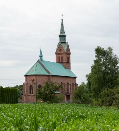 Zdjęcie nr 48: Kościół ceglany, na planie prostokąta z węższym i niższym prezbiterium z zakrystią od północy i wieżą od zachodu. Kościół orientowany, jednonawowy, czteroprzęsłowy z węższym, jednoprzęsłowym prezbiterium zamkniętym trójbocznie, z kruchtą w przyziemiu wieży. Nawa artykułowana półfilarami o ściętych narożach, przechodzącymi w zamknięte łukiem ostrym gurty krzyżowo-żebrowego sklepienia. W nawie i prezbiterium okna prostokątne zamknięte łukiem ostrym – pięć w prezbiterium, po trzy z każdej strony nawy. Węższe okna w przęśle chóru, kolejne w fasadzie. Główne wejście od wschodu, drugie od zachodu. Chór muzyczny w czwartym przęśle nawy, wsparty na wielobocznych filarach, podtrzymujących ostrołukowe arkady, z parapetem ozdobionym blendami. Ściany w dolnej partii pokryte drewnianą boazerią, wyżej malowane na kremowo, w partiach sklepienia polichromia podkreślająca elementy konstrukcji fragmentami stylizowanej wici i dekoracji floralnej; na belce tęczowej anioły niosące plakiety z symbolami świętych sakramentów. Fasada trójosiowa, z ryzalitem szerokości wieży oszkarpowanym na narożach. Podziały poziome przeprowadzone przy pomocy gzymsów. Na osi ostrołukowe wejście, powyżej wypełniony maswerkiem okulus. Następna kondygnacja jest częścią czworobocznej wieży, wypełniono ją dużym oknem w kształcę stojącego prostokąta zamkniętego łukiem ostrym.  Boczne osie z małymi oknami powtarzającymi kształt pozostałych, zamknięte trójkątnym przyczółkiem przerwanym na wieżę. Najwyższa kondygnacja wieży przepruta z każdej strony parą okien w kształcie stojących prostokątów umieszczonych w ostrołukowych niszach. Wieńczący ją gzyms dekorowany zygzakiem, powyżej trójkątne szczyty z ostrołukową blendą z okulusem w centrum. Elewacje boczne i prezbiterium oszkarpowane, przeprute oknami.  Hełm wieży w formie latarni zakończonej stożkiem z kupą i krzyżem, nawa przekryta dachem dwuspadowym, prezbiterium wielobocznym, zakrystia i wejście od zachodu pulpitowymi. 


Do najciekawszych elementów wyposażenia należą zespół neogotyckich ołtarzy wraz z amboną oraz kolekcja dziewiętnastowiecznych feretronów. W otoczeniu kościoła znajduje się kamienna figura św. Jana Nepomucena z 1788 roku. 
