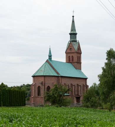 Zdjęcie nr 49: Kościół ceglany, na planie prostokąta z węższym i niższym prezbiterium z zakrystią od północy i wieżą od zachodu. Kościół orientowany, jednonawowy, czteroprzęsłowy z węższym, jednoprzęsłowym prezbiterium zamkniętym trójbocznie, z kruchtą w przyziemiu wieży. Nawa artykułowana półfilarami o ściętych narożach, przechodzącymi w zamknięte łukiem ostrym gurty krzyżowo-żebrowego sklepienia. W nawie i prezbiterium okna prostokątne zamknięte łukiem ostrym – pięć w prezbiterium, po trzy z każdej strony nawy. Węższe okna w przęśle chóru, kolejne w fasadzie. Główne wejście od wschodu, drugie od zachodu. Chór muzyczny w czwartym przęśle nawy, wsparty na wielobocznych filarach, podtrzymujących ostrołukowe arkady, z parapetem ozdobionym blendami. Ściany w dolnej partii pokryte drewnianą boazerią, wyżej malowane na kremowo, w partiach sklepienia polichromia podkreślająca elementy konstrukcji fragmentami stylizowanej wici i dekoracji floralnej; na belce tęczowej anioły niosące plakiety z symbolami świętych sakramentów. Fasada trójosiowa, z ryzalitem szerokości wieży oszkarpowanym na narożach. Podziały poziome przeprowadzone przy pomocy gzymsów. Na osi ostrołukowe wejście, powyżej wypełniony maswerkiem okulus. Następna kondygnacja jest częścią czworobocznej wieży, wypełniono ją dużym oknem w kształcę stojącego prostokąta zamkniętego łukiem ostrym.  Boczne osie z małymi oknami powtarzającymi kształt pozostałych, zamknięte trójkątnym przyczółkiem przerwanym na wieżę. Najwyższa kondygnacja wieży przepruta z każdej strony parą okien w kształcie stojących prostokątów umieszczonych w ostrołukowych niszach. Wieńczący ją gzyms dekorowany zygzakiem, powyżej trójkątne szczyty z ostrołukową blendą z okulusem w centrum. Elewacje boczne i prezbiterium oszkarpowane, przeprute oknami.  Hełm wieży w formie latarni zakończonej stożkiem z kupą i krzyżem, nawa przekryta dachem dwuspadowym, prezbiterium wielobocznym, zakrystia i wejście od zachodu pulpitowymi. 


Do najciekawszych elementów wyposażenia należą zespół neogotyckich ołtarzy wraz z amboną oraz kolekcja dziewiętnastowiecznych feretronów. W otoczeniu kościoła znajduje się kamienna figura św. Jana Nepomucena z 1788 roku. 
