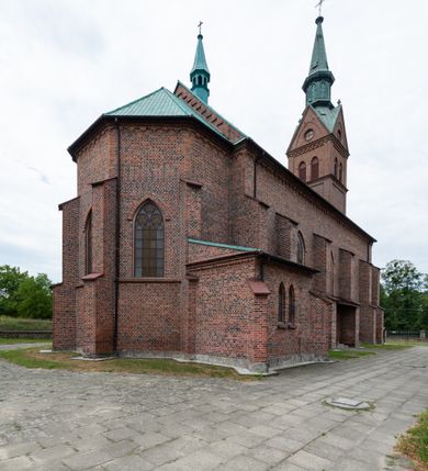 Zdjęcie nr 4: Kościół ceglany, na planie prostokąta z węższym i niższym prezbiterium z zakrystią od północy i wieżą od zachodu. Kościół orientowany, jednonawowy, czteroprzęsłowy z węższym, jednoprzęsłowym prezbiterium zamkniętym trójbocznie, z kruchtą w przyziemiu wieży. Nawa artykułowana półfilarami o ściętych narożach, przechodzącymi w zamknięte łukiem ostrym gurty krzyżowo-żebrowego sklepienia. W nawie i prezbiterium okna prostokątne zamknięte łukiem ostrym – pięć w prezbiterium, po trzy z każdej strony nawy. Węższe okna w przęśle chóru, kolejne w fasadzie. Główne wejście od wschodu, drugie od zachodu. Chór muzyczny w czwartym przęśle nawy, wsparty na wielobocznych filarach, podtrzymujących ostrołukowe arkady, z parapetem ozdobionym blendami. Ściany w dolnej partii pokryte drewnianą boazerią, wyżej malowane na kremowo, w partiach sklepienia polichromia podkreślająca elementy konstrukcji fragmentami stylizowanej wici i dekoracji floralnej; na belce tęczowej anioły niosące plakiety z symbolami świętych sakramentów. Fasada trójosiowa, z ryzalitem szerokości wieży oszkarpowanym na narożach. Podziały poziome przeprowadzone przy pomocy gzymsów. Na osi ostrołukowe wejście, powyżej wypełniony maswerkiem okulus. Następna kondygnacja jest częścią czworobocznej wieży, wypełniono ją dużym oknem w kształcę stojącego prostokąta zamkniętego łukiem ostrym.  Boczne osie z małymi oknami powtarzającymi kształt pozostałych, zamknięte trójkątnym przyczółkiem przerwanym na wieżę. Najwyższa kondygnacja wieży przepruta z każdej strony parą okien w kształcie stojących prostokątów umieszczonych w ostrołukowych niszach. Wieńczący ją gzyms dekorowany zygzakiem, powyżej trójkątne szczyty z ostrołukową blendą z okulusem w centrum. Elewacje boczne i prezbiterium oszkarpowane, przeprute oknami.  Hełm wieży w formie latarni zakończonej stożkiem z kupą i krzyżem, nawa przekryta dachem dwuspadowym, prezbiterium wielobocznym, zakrystia i wejście od zachodu pulpitowymi. 


Do najciekawszych elementów wyposażenia należą zespół neogotyckich ołtarzy wraz z amboną oraz kolekcja dziewiętnastowiecznych feretronów. W otoczeniu kościoła znajduje się kamienna figura św. Jana Nepomucena z 1788 roku. 
