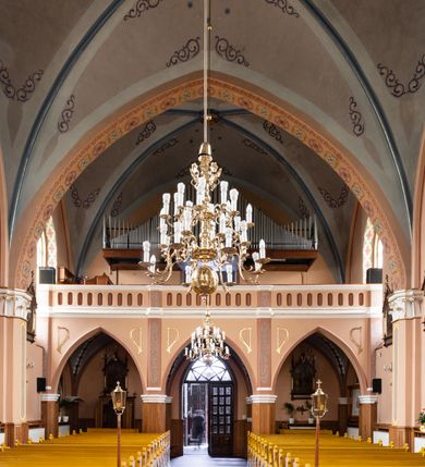 Zdjęcie nr 18: Kościół ceglany, na planie prostokąta z węższym i niższym prezbiterium z zakrystią od północy i wieżą od zachodu. Kościół orientowany, jednonawowy, czteroprzęsłowy z węższym, jednoprzęsłowym prezbiterium zamkniętym trójbocznie, z kruchtą w przyziemiu wieży. Nawa artykułowana półfilarami o ściętych narożach, przechodzącymi w zamknięte łukiem ostrym gurty krzyżowo-żebrowego sklepienia. W nawie i prezbiterium okna prostokątne zamknięte łukiem ostrym – pięć w prezbiterium, po trzy z każdej strony nawy. Węższe okna w przęśle chóru, kolejne w fasadzie. Główne wejście od wschodu, drugie od zachodu. Chór muzyczny w czwartym przęśle nawy, wsparty na wielobocznych filarach, podtrzymujących ostrołukowe arkady, z parapetem ozdobionym blendami. Ściany w dolnej partii pokryte drewnianą boazerią, wyżej malowane na kremowo, w partiach sklepienia polichromia podkreślająca elementy konstrukcji fragmentami stylizowanej wici i dekoracji floralnej; na belce tęczowej anioły niosące plakiety z symbolami świętych sakramentów. Fasada trójosiowa, z ryzalitem szerokości wieży oszkarpowanym na narożach. Podziały poziome przeprowadzone przy pomocy gzymsów. Na osi ostrołukowe wejście, powyżej wypełniony maswerkiem okulus. Następna kondygnacja jest częścią czworobocznej wieży, wypełniono ją dużym oknem w kształcę stojącego prostokąta zamkniętego łukiem ostrym.  Boczne osie z małymi oknami powtarzającymi kształt pozostałych, zamknięte trójkątnym przyczółkiem przerwanym na wieżę. Najwyższa kondygnacja wieży przepruta z każdej strony parą okien w kształcie stojących prostokątów umieszczonych w ostrołukowych niszach. Wieńczący ją gzyms dekorowany zygzakiem, powyżej trójkątne szczyty z ostrołukową blendą z okulusem w centrum. Elewacje boczne i prezbiterium oszkarpowane, przeprute oknami.  Hełm wieży w formie latarni zakończonej stożkiem z kupą i krzyżem, nawa przekryta dachem dwuspadowym, prezbiterium wielobocznym, zakrystia i wejście od zachodu pulpitowymi. 


Do najciekawszych elementów wyposażenia należą zespół neogotyckich ołtarzy wraz z amboną oraz kolekcja dziewiętnastowiecznych feretronów. W otoczeniu kościoła znajduje się kamienna figura św. Jana Nepomucena z 1788 roku. 
