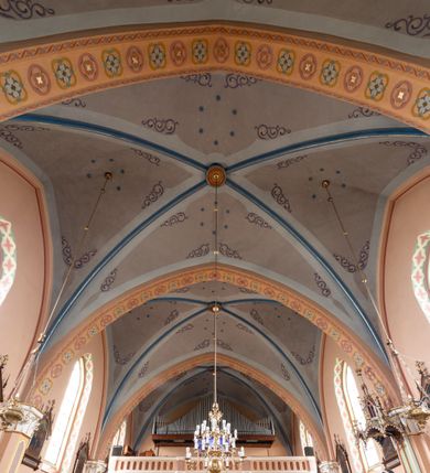 Zdjęcie nr 12: Kościół ceglany, na planie prostokąta z węższym i niższym prezbiterium z zakrystią od północy i wieżą od zachodu. Kościół orientowany, jednonawowy, czteroprzęsłowy z węższym, jednoprzęsłowym prezbiterium zamkniętym trójbocznie, z kruchtą w przyziemiu wieży. Nawa artykułowana półfilarami o ściętych narożach, przechodzącymi w zamknięte łukiem ostrym gurty krzyżowo-żebrowego sklepienia. W nawie i prezbiterium okna prostokątne zamknięte łukiem ostrym – pięć w prezbiterium, po trzy z każdej strony nawy. Węższe okna w przęśle chóru, kolejne w fasadzie. Główne wejście od wschodu, drugie od zachodu. Chór muzyczny w czwartym przęśle nawy, wsparty na wielobocznych filarach, podtrzymujących ostrołukowe arkady, z parapetem ozdobionym blendami. Ściany w dolnej partii pokryte drewnianą boazerią, wyżej malowane na kremowo, w partiach sklepienia polichromia podkreślająca elementy konstrukcji fragmentami stylizowanej wici i dekoracji floralnej; na belce tęczowej anioły niosące plakiety z symbolami świętych sakramentów. Fasada trójosiowa, z ryzalitem szerokości wieży oszkarpowanym na narożach. Podziały poziome przeprowadzone przy pomocy gzymsów. Na osi ostrołukowe wejście, powyżej wypełniony maswerkiem okulus. Następna kondygnacja jest częścią czworobocznej wieży, wypełniono ją dużym oknem w kształcę stojącego prostokąta zamkniętego łukiem ostrym.  Boczne osie z małymi oknami powtarzającymi kształt pozostałych, zamknięte trójkątnym przyczółkiem przerwanym na wieżę. Najwyższa kondygnacja wieży przepruta z każdej strony parą okien w kształcie stojących prostokątów umieszczonych w ostrołukowych niszach. Wieńczący ją gzyms dekorowany zygzakiem, powyżej trójkątne szczyty z ostrołukową blendą z okulusem w centrum. Elewacje boczne i prezbiterium oszkarpowane, przeprute oknami.  Hełm wieży w formie latarni zakończonej stożkiem z kupą i krzyżem, nawa przekryta dachem dwuspadowym, prezbiterium wielobocznym, zakrystia i wejście od zachodu pulpitowymi. 


Do najciekawszych elementów wyposażenia należą zespół neogotyckich ołtarzy wraz z amboną oraz kolekcja dziewiętnastowiecznych feretronów. W otoczeniu kościoła znajduje się kamienna figura św. Jana Nepomucena z 1788 roku. 
