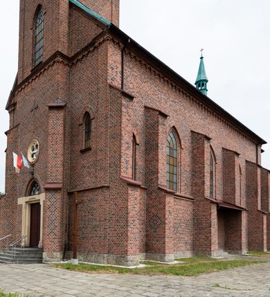 Zdjęcie nr 14: Kościół ceglany, na planie prostokąta z węższym i niższym prezbiterium z zakrystią od północy i wieżą od zachodu. Kościół orientowany, jednonawowy, czteroprzęsłowy z węższym, jednoprzęsłowym prezbiterium zamkniętym trójbocznie, z kruchtą w przyziemiu wieży. Nawa artykułowana półfilarami o ściętych narożach, przechodzącymi w zamknięte łukiem ostrym gurty krzyżowo-żebrowego sklepienia. W nawie i prezbiterium okna prostokątne zamknięte łukiem ostrym – pięć w prezbiterium, po trzy z każdej strony nawy. Węższe okna w przęśle chóru, kolejne w fasadzie. Główne wejście od wschodu, drugie od zachodu. Chór muzyczny w czwartym przęśle nawy, wsparty na wielobocznych filarach, podtrzymujących ostrołukowe arkady, z parapetem ozdobionym blendami. Ściany w dolnej partii pokryte drewnianą boazerią, wyżej malowane na kremowo, w partiach sklepienia polichromia podkreślająca elementy konstrukcji fragmentami stylizowanej wici i dekoracji floralnej; na belce tęczowej anioły niosące plakiety z symbolami świętych sakramentów. Fasada trójosiowa, z ryzalitem szerokości wieży oszkarpowanym na narożach. Podziały poziome przeprowadzone przy pomocy gzymsów. Na osi ostrołukowe wejście, powyżej wypełniony maswerkiem okulus. Następna kondygnacja jest częścią czworobocznej wieży, wypełniono ją dużym oknem w kształcę stojącego prostokąta zamkniętego łukiem ostrym.  Boczne osie z małymi oknami powtarzającymi kształt pozostałych, zamknięte trójkątnym przyczółkiem przerwanym na wieżę. Najwyższa kondygnacja wieży przepruta z każdej strony parą okien w kształcie stojących prostokątów umieszczonych w ostrołukowych niszach. Wieńczący ją gzyms dekorowany zygzakiem, powyżej trójkątne szczyty z ostrołukową blendą z okulusem w centrum. Elewacje boczne i prezbiterium oszkarpowane, przeprute oknami.  Hełm wieży w formie latarni zakończonej stożkiem z kupą i krzyżem, nawa przekryta dachem dwuspadowym, prezbiterium wielobocznym, zakrystia i wejście od zachodu pulpitowymi. 


Do najciekawszych elementów wyposażenia należą zespół neogotyckich ołtarzy wraz z amboną oraz kolekcja dziewiętnastowiecznych feretronów. W otoczeniu kościoła znajduje się kamienna figura św. Jana Nepomucena z 1788 roku. 
