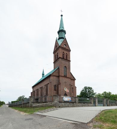 Zdjęcie nr 15: Kościół ceglany, na planie prostokąta z węższym i niższym prezbiterium z zakrystią od północy i wieżą od zachodu. Kościół orientowany, jednonawowy, czteroprzęsłowy z węższym, jednoprzęsłowym prezbiterium zamkniętym trójbocznie, z kruchtą w przyziemiu wieży. Nawa artykułowana półfilarami o ściętych narożach, przechodzącymi w zamknięte łukiem ostrym gurty krzyżowo-żebrowego sklepienia. W nawie i prezbiterium okna prostokątne zamknięte łukiem ostrym – pięć w prezbiterium, po trzy z każdej strony nawy. Węższe okna w przęśle chóru, kolejne w fasadzie. Główne wejście od wschodu, drugie od zachodu. Chór muzyczny w czwartym przęśle nawy, wsparty na wielobocznych filarach, podtrzymujących ostrołukowe arkady, z parapetem ozdobionym blendami. Ściany w dolnej partii pokryte drewnianą boazerią, wyżej malowane na kremowo, w partiach sklepienia polichromia podkreślająca elementy konstrukcji fragmentami stylizowanej wici i dekoracji floralnej; na belce tęczowej anioły niosące plakiety z symbolami świętych sakramentów. Fasada trójosiowa, z ryzalitem szerokości wieży oszkarpowanym na narożach. Podziały poziome przeprowadzone przy pomocy gzymsów. Na osi ostrołukowe wejście, powyżej wypełniony maswerkiem okulus. Następna kondygnacja jest częścią czworobocznej wieży, wypełniono ją dużym oknem w kształcę stojącego prostokąta zamkniętego łukiem ostrym.  Boczne osie z małymi oknami powtarzającymi kształt pozostałych, zamknięte trójkątnym przyczółkiem przerwanym na wieżę. Najwyższa kondygnacja wieży przepruta z każdej strony parą okien w kształcie stojących prostokątów umieszczonych w ostrołukowych niszach. Wieńczący ją gzyms dekorowany zygzakiem, powyżej trójkątne szczyty z ostrołukową blendą z okulusem w centrum. Elewacje boczne i prezbiterium oszkarpowane, przeprute oknami.  Hełm wieży w formie latarni zakończonej stożkiem z kupą i krzyżem, nawa przekryta dachem dwuspadowym, prezbiterium wielobocznym, zakrystia i wejście od zachodu pulpitowymi. 


Do najciekawszych elementów wyposażenia należą zespół neogotyckich ołtarzy wraz z amboną oraz kolekcja dziewiętnastowiecznych feretronów. W otoczeniu kościoła znajduje się kamienna figura św. Jana Nepomucena z 1788 roku. 
