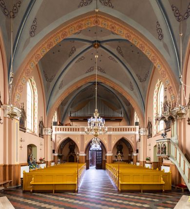 Zdjęcie nr 22: Kościół ceglany, na planie prostokąta z węższym i niższym prezbiterium z zakrystią od północy i wieżą od zachodu. Kościół orientowany, jednonawowy, czteroprzęsłowy z węższym, jednoprzęsłowym prezbiterium zamkniętym trójbocznie, z kruchtą w przyziemiu wieży. Nawa artykułowana półfilarami o ściętych narożach, przechodzącymi w zamknięte łukiem ostrym gurty krzyżowo-żebrowego sklepienia. W nawie i prezbiterium okna prostokątne zamknięte łukiem ostrym – pięć w prezbiterium, po trzy z każdej strony nawy. Węższe okna w przęśle chóru, kolejne w fasadzie. Główne wejście od wschodu, drugie od zachodu. Chór muzyczny w czwartym przęśle nawy, wsparty na wielobocznych filarach, podtrzymujących ostrołukowe arkady, z parapetem ozdobionym blendami. Ściany w dolnej partii pokryte drewnianą boazerią, wyżej malowane na kremowo, w partiach sklepienia polichromia podkreślająca elementy konstrukcji fragmentami stylizowanej wici i dekoracji floralnej; na belce tęczowej anioły niosące plakiety z symbolami świętych sakramentów. Fasada trójosiowa, z ryzalitem szerokości wieży oszkarpowanym na narożach. Podziały poziome przeprowadzone przy pomocy gzymsów. Na osi ostrołukowe wejście, powyżej wypełniony maswerkiem okulus. Następna kondygnacja jest częścią czworobocznej wieży, wypełniono ją dużym oknem w kształcę stojącego prostokąta zamkniętego łukiem ostrym.  Boczne osie z małymi oknami powtarzającymi kształt pozostałych, zamknięte trójkątnym przyczółkiem przerwanym na wieżę. Najwyższa kondygnacja wieży przepruta z każdej strony parą okien w kształcie stojących prostokątów umieszczonych w ostrołukowych niszach. Wieńczący ją gzyms dekorowany zygzakiem, powyżej trójkątne szczyty z ostrołukową blendą z okulusem w centrum. Elewacje boczne i prezbiterium oszkarpowane, przeprute oknami.  Hełm wieży w formie latarni zakończonej stożkiem z kupą i krzyżem, nawa przekryta dachem dwuspadowym, prezbiterium wielobocznym, zakrystia i wejście od zachodu pulpitowymi. 


Do najciekawszych elementów wyposażenia należą zespół neogotyckich ołtarzy wraz z amboną oraz kolekcja dziewiętnastowiecznych feretronów. W otoczeniu kościoła znajduje się kamienna figura św. Jana Nepomucena z 1788 roku. 
