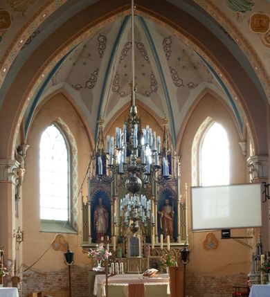 Zdjęcie nr 27: Kościół ceglany, na planie prostokąta z węższym i niższym prezbiterium z zakrystią od północy i wieżą od zachodu. Kościół orientowany, jednonawowy, czteroprzęsłowy z węższym, jednoprzęsłowym prezbiterium zamkniętym trójbocznie, z kruchtą w przyziemiu wieży. Nawa artykułowana półfilarami o ściętych narożach, przechodzącymi w zamknięte łukiem ostrym gurty krzyżowo-żebrowego sklepienia. W nawie i prezbiterium okna prostokątne zamknięte łukiem ostrym – pięć w prezbiterium, po trzy z każdej strony nawy. Węższe okna w przęśle chóru, kolejne w fasadzie. Główne wejście od wschodu, drugie od zachodu. Chór muzyczny w czwartym przęśle nawy, wsparty na wielobocznych filarach, podtrzymujących ostrołukowe arkady, z parapetem ozdobionym blendami. Ściany w dolnej partii pokryte drewnianą boazerią, wyżej malowane na kremowo, w partiach sklepienia polichromia podkreślająca elementy konstrukcji fragmentami stylizowanej wici i dekoracji floralnej; na belce tęczowej anioły niosące plakiety z symbolami świętych sakramentów. Fasada trójosiowa, z ryzalitem szerokości wieży oszkarpowanym na narożach. Podziały poziome przeprowadzone przy pomocy gzymsów. Na osi ostrołukowe wejście, powyżej wypełniony maswerkiem okulus. Następna kondygnacja jest częścią czworobocznej wieży, wypełniono ją dużym oknem w kształcę stojącego prostokąta zamkniętego łukiem ostrym.  Boczne osie z małymi oknami powtarzającymi kształt pozostałych, zamknięte trójkątnym przyczółkiem przerwanym na wieżę. Najwyższa kondygnacja wieży przepruta z każdej strony parą okien w kształcie stojących prostokątów umieszczonych w ostrołukowych niszach. Wieńczący ją gzyms dekorowany zygzakiem, powyżej trójkątne szczyty z ostrołukową blendą z okulusem w centrum. Elewacje boczne i prezbiterium oszkarpowane, przeprute oknami.  Hełm wieży w formie latarni zakończonej stożkiem z kupą i krzyżem, nawa przekryta dachem dwuspadowym, prezbiterium wielobocznym, zakrystia i wejście od zachodu pulpitowymi. 


Do najciekawszych elementów wyposażenia należą zespół neogotyckich ołtarzy wraz z amboną oraz kolekcja dziewiętnastowiecznych feretronów. W otoczeniu kościoła znajduje się kamienna figura św. Jana Nepomucena z 1788 roku. 
