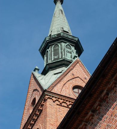 Zdjęcie nr 32: Kościół ceglany, na planie prostokąta z węższym i niższym prezbiterium z zakrystią od północy i wieżą od zachodu. Kościół orientowany, jednonawowy, czteroprzęsłowy z węższym, jednoprzęsłowym prezbiterium zamkniętym trójbocznie, z kruchtą w przyziemiu wieży. Nawa artykułowana półfilarami o ściętych narożach, przechodzącymi w zamknięte łukiem ostrym gurty krzyżowo-żebrowego sklepienia. W nawie i prezbiterium okna prostokątne zamknięte łukiem ostrym – pięć w prezbiterium, po trzy z każdej strony nawy. Węższe okna w przęśle chóru, kolejne w fasadzie. Główne wejście od wschodu, drugie od zachodu. Chór muzyczny w czwartym przęśle nawy, wsparty na wielobocznych filarach, podtrzymujących ostrołukowe arkady, z parapetem ozdobionym blendami. Ściany w dolnej partii pokryte drewnianą boazerią, wyżej malowane na kremowo, w partiach sklepienia polichromia podkreślająca elementy konstrukcji fragmentami stylizowanej wici i dekoracji floralnej; na belce tęczowej anioły niosące plakiety z symbolami świętych sakramentów. Fasada trójosiowa, z ryzalitem szerokości wieży oszkarpowanym na narożach. Podziały poziome przeprowadzone przy pomocy gzymsów. Na osi ostrołukowe wejście, powyżej wypełniony maswerkiem okulus. Następna kondygnacja jest częścią czworobocznej wieży, wypełniono ją dużym oknem w kształcę stojącego prostokąta zamkniętego łukiem ostrym.  Boczne osie z małymi oknami powtarzającymi kształt pozostałych, zamknięte trójkątnym przyczółkiem przerwanym na wieżę. Najwyższa kondygnacja wieży przepruta z każdej strony parą okien w kształcie stojących prostokątów umieszczonych w ostrołukowych niszach. Wieńczący ją gzyms dekorowany zygzakiem, powyżej trójkątne szczyty z ostrołukową blendą z okulusem w centrum. Elewacje boczne i prezbiterium oszkarpowane, przeprute oknami.  Hełm wieży w formie latarni zakończonej stożkiem z kupą i krzyżem, nawa przekryta dachem dwuspadowym, prezbiterium wielobocznym, zakrystia i wejście od zachodu pulpitowymi. 


Do najciekawszych elementów wyposażenia należą zespół neogotyckich ołtarzy wraz z amboną oraz kolekcja dziewiętnastowiecznych feretronów. W otoczeniu kościoła znajduje się kamienna figura św. Jana Nepomucena z 1788 roku. 
