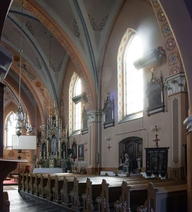 Zdjęcie nr 28: Kościół ceglany, na planie prostokąta z węższym i niższym prezbiterium z zakrystią od północy i wieżą od zachodu. Kościół orientowany, jednonawowy, czteroprzęsłowy z węższym, jednoprzęsłowym prezbiterium zamkniętym trójbocznie, z kruchtą w przyziemiu wieży. Nawa artykułowana półfilarami o ściętych narożach, przechodzącymi w zamknięte łukiem ostrym gurty krzyżowo-żebrowego sklepienia. W nawie i prezbiterium okna prostokątne zamknięte łukiem ostrym – pięć w prezbiterium, po trzy z każdej strony nawy. Węższe okna w przęśle chóru, kolejne w fasadzie. Główne wejście od wschodu, drugie od zachodu. Chór muzyczny w czwartym przęśle nawy, wsparty na wielobocznych filarach, podtrzymujących ostrołukowe arkady, z parapetem ozdobionym blendami. Ściany w dolnej partii pokryte drewnianą boazerią, wyżej malowane na kremowo, w partiach sklepienia polichromia podkreślająca elementy konstrukcji fragmentami stylizowanej wici i dekoracji floralnej; na belce tęczowej anioły niosące plakiety z symbolami świętych sakramentów. Fasada trójosiowa, z ryzalitem szerokości wieży oszkarpowanym na narożach. Podziały poziome przeprowadzone przy pomocy gzymsów. Na osi ostrołukowe wejście, powyżej wypełniony maswerkiem okulus. Następna kondygnacja jest częścią czworobocznej wieży, wypełniono ją dużym oknem w kształcę stojącego prostokąta zamkniętego łukiem ostrym.  Boczne osie z małymi oknami powtarzającymi kształt pozostałych, zamknięte trójkątnym przyczółkiem przerwanym na wieżę. Najwyższa kondygnacja wieży przepruta z każdej strony parą okien w kształcie stojących prostokątów umieszczonych w ostrołukowych niszach. Wieńczący ją gzyms dekorowany zygzakiem, powyżej trójkątne szczyty z ostrołukową blendą z okulusem w centrum. Elewacje boczne i prezbiterium oszkarpowane, przeprute oknami.  Hełm wieży w formie latarni zakończonej stożkiem z kupą i krzyżem, nawa przekryta dachem dwuspadowym, prezbiterium wielobocznym, zakrystia i wejście od zachodu pulpitowymi. 


Do najciekawszych elementów wyposażenia należą zespół neogotyckich ołtarzy wraz z amboną oraz kolekcja dziewiętnastowiecznych feretronów. W otoczeniu kościoła znajduje się kamienna figura św. Jana Nepomucena z 1788 roku. 
