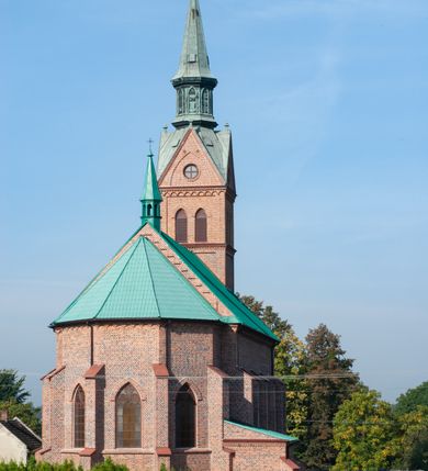 Zdjęcie nr 29: Kościół ceglany, na planie prostokąta z węższym i niższym prezbiterium z zakrystią od północy i wieżą od zachodu. Kościół orientowany, jednonawowy, czteroprzęsłowy z węższym, jednoprzęsłowym prezbiterium zamkniętym trójbocznie, z kruchtą w przyziemiu wieży. Nawa artykułowana półfilarami o ściętych narożach, przechodzącymi w zamknięte łukiem ostrym gurty krzyżowo-żebrowego sklepienia. W nawie i prezbiterium okna prostokątne zamknięte łukiem ostrym – pięć w prezbiterium, po trzy z każdej strony nawy. Węższe okna w przęśle chóru, kolejne w fasadzie. Główne wejście od wschodu, drugie od zachodu. Chór muzyczny w czwartym przęśle nawy, wsparty na wielobocznych filarach, podtrzymujących ostrołukowe arkady, z parapetem ozdobionym blendami. Ściany w dolnej partii pokryte drewnianą boazerią, wyżej malowane na kremowo, w partiach sklepienia polichromia podkreślająca elementy konstrukcji fragmentami stylizowanej wici i dekoracji floralnej; na belce tęczowej anioły niosące plakiety z symbolami świętych sakramentów. Fasada trójosiowa, z ryzalitem szerokości wieży oszkarpowanym na narożach. Podziały poziome przeprowadzone przy pomocy gzymsów. Na osi ostrołukowe wejście, powyżej wypełniony maswerkiem okulus. Następna kondygnacja jest częścią czworobocznej wieży, wypełniono ją dużym oknem w kształcę stojącego prostokąta zamkniętego łukiem ostrym.  Boczne osie z małymi oknami powtarzającymi kształt pozostałych, zamknięte trójkątnym przyczółkiem przerwanym na wieżę. Najwyższa kondygnacja wieży przepruta z każdej strony parą okien w kształcie stojących prostokątów umieszczonych w ostrołukowych niszach. Wieńczący ją gzyms dekorowany zygzakiem, powyżej trójkątne szczyty z ostrołukową blendą z okulusem w centrum. Elewacje boczne i prezbiterium oszkarpowane, przeprute oknami.  Hełm wieży w formie latarni zakończonej stożkiem z kupą i krzyżem, nawa przekryta dachem dwuspadowym, prezbiterium wielobocznym, zakrystia i wejście od zachodu pulpitowymi. 


Do najciekawszych elementów wyposażenia należą zespół neogotyckich ołtarzy wraz z amboną oraz kolekcja dziewiętnastowiecznych feretronów. W otoczeniu kościoła znajduje się kamienna figura św. Jana Nepomucena z 1788 roku. 
