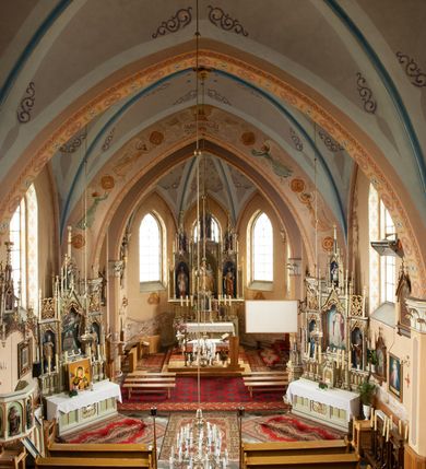 Zdjęcie nr 33: Kościół ceglany, na planie prostokąta z węższym i niższym prezbiterium z zakrystią od północy i wieżą od zachodu. Kościół orientowany, jednonawowy, czteroprzęsłowy z węższym, jednoprzęsłowym prezbiterium zamkniętym trójbocznie, z kruchtą w przyziemiu wieży. Nawa artykułowana półfilarami o ściętych narożach, przechodzącymi w zamknięte łukiem ostrym gurty krzyżowo-żebrowego sklepienia. W nawie i prezbiterium okna prostokątne zamknięte łukiem ostrym – pięć w prezbiterium, po trzy z każdej strony nawy. Węższe okna w przęśle chóru, kolejne w fasadzie. Główne wejście od wschodu, drugie od zachodu. Chór muzyczny w czwartym przęśle nawy, wsparty na wielobocznych filarach, podtrzymujących ostrołukowe arkady, z parapetem ozdobionym blendami. Ściany w dolnej partii pokryte drewnianą boazerią, wyżej malowane na kremowo, w partiach sklepienia polichromia podkreślająca elementy konstrukcji fragmentami stylizowanej wici i dekoracji floralnej; na belce tęczowej anioły niosące plakiety z symbolami świętych sakramentów. Fasada trójosiowa, z ryzalitem szerokości wieży oszkarpowanym na narożach. Podziały poziome przeprowadzone przy pomocy gzymsów. Na osi ostrołukowe wejście, powyżej wypełniony maswerkiem okulus. Następna kondygnacja jest częścią czworobocznej wieży, wypełniono ją dużym oknem w kształcę stojącego prostokąta zamkniętego łukiem ostrym.  Boczne osie z małymi oknami powtarzającymi kształt pozostałych, zamknięte trójkątnym przyczółkiem przerwanym na wieżę. Najwyższa kondygnacja wieży przepruta z każdej strony parą okien w kształcie stojących prostokątów umieszczonych w ostrołukowych niszach. Wieńczący ją gzyms dekorowany zygzakiem, powyżej trójkątne szczyty z ostrołukową blendą z okulusem w centrum. Elewacje boczne i prezbiterium oszkarpowane, przeprute oknami.  Hełm wieży w formie latarni zakończonej stożkiem z kupą i krzyżem, nawa przekryta dachem dwuspadowym, prezbiterium wielobocznym, zakrystia i wejście od zachodu pulpitowymi. 


Do najciekawszych elementów wyposażenia należą zespół neogotyckich ołtarzy wraz z amboną oraz kolekcja dziewiętnastowiecznych feretronów. W otoczeniu kościoła znajduje się kamienna figura św. Jana Nepomucena z 1788 roku. 
