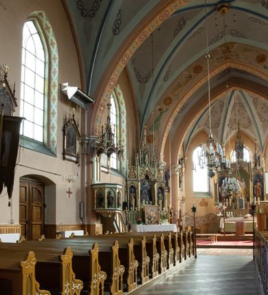 Zdjęcie nr 43: Kościół ceglany, na planie prostokąta z węższym i niższym prezbiterium z zakrystią od północy i wieżą od zachodu. Kościół orientowany, jednonawowy, czteroprzęsłowy z węższym, jednoprzęsłowym prezbiterium zamkniętym trójbocznie, z kruchtą w przyziemiu wieży. Nawa artykułowana półfilarami o ściętych narożach, przechodzącymi w zamknięte łukiem ostrym gurty krzyżowo-żebrowego sklepienia. W nawie i prezbiterium okna prostokątne zamknięte łukiem ostrym – pięć w prezbiterium, po trzy z każdej strony nawy. Węższe okna w przęśle chóru, kolejne w fasadzie. Główne wejście od wschodu, drugie od zachodu. Chór muzyczny w czwartym przęśle nawy, wsparty na wielobocznych filarach, podtrzymujących ostrołukowe arkady, z parapetem ozdobionym blendami. Ściany w dolnej partii pokryte drewnianą boazerią, wyżej malowane na kremowo, w partiach sklepienia polichromia podkreślająca elementy konstrukcji fragmentami stylizowanej wici i dekoracji floralnej; na belce tęczowej anioły niosące plakiety z symbolami świętych sakramentów. Fasada trójosiowa, z ryzalitem szerokości wieży oszkarpowanym na narożach. Podziały poziome przeprowadzone przy pomocy gzymsów. Na osi ostrołukowe wejście, powyżej wypełniony maswerkiem okulus. Następna kondygnacja jest częścią czworobocznej wieży, wypełniono ją dużym oknem w kształcę stojącego prostokąta zamkniętego łukiem ostrym.  Boczne osie z małymi oknami powtarzającymi kształt pozostałych, zamknięte trójkątnym przyczółkiem przerwanym na wieżę. Najwyższa kondygnacja wieży przepruta z każdej strony parą okien w kształcie stojących prostokątów umieszczonych w ostrołukowych niszach. Wieńczący ją gzyms dekorowany zygzakiem, powyżej trójkątne szczyty z ostrołukową blendą z okulusem w centrum. Elewacje boczne i prezbiterium oszkarpowane, przeprute oknami.  Hełm wieży w formie latarni zakończonej stożkiem z kupą i krzyżem, nawa przekryta dachem dwuspadowym, prezbiterium wielobocznym, zakrystia i wejście od zachodu pulpitowymi. 


Do najciekawszych elementów wyposażenia należą zespół neogotyckich ołtarzy wraz z amboną oraz kolekcja dziewiętnastowiecznych feretronów. W otoczeniu kościoła znajduje się kamienna figura św. Jana Nepomucena z 1788 roku. 
