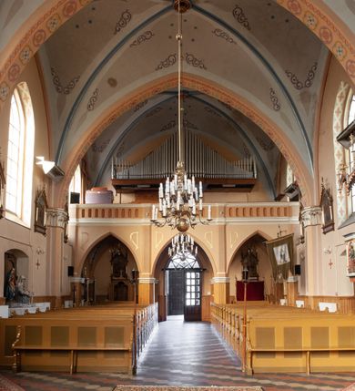 Zdjęcie nr 44: Kościół ceglany, na planie prostokąta z węższym i niższym prezbiterium z zakrystią od północy i wieżą od zachodu. Kościół orientowany, jednonawowy, czteroprzęsłowy z węższym, jednoprzęsłowym prezbiterium zamkniętym trójbocznie, z kruchtą w przyziemiu wieży. Nawa artykułowana półfilarami o ściętych narożach, przechodzącymi w zamknięte łukiem ostrym gurty krzyżowo-żebrowego sklepienia. W nawie i prezbiterium okna prostokątne zamknięte łukiem ostrym – pięć w prezbiterium, po trzy z każdej strony nawy. Węższe okna w przęśle chóru, kolejne w fasadzie. Główne wejście od wschodu, drugie od zachodu. Chór muzyczny w czwartym przęśle nawy, wsparty na wielobocznych filarach, podtrzymujących ostrołukowe arkady, z parapetem ozdobionym blendami. Ściany w dolnej partii pokryte drewnianą boazerią, wyżej malowane na kremowo, w partiach sklepienia polichromia podkreślająca elementy konstrukcji fragmentami stylizowanej wici i dekoracji floralnej; na belce tęczowej anioły niosące plakiety z symbolami świętych sakramentów. Fasada trójosiowa, z ryzalitem szerokości wieży oszkarpowanym na narożach. Podziały poziome przeprowadzone przy pomocy gzymsów. Na osi ostrołukowe wejście, powyżej wypełniony maswerkiem okulus. Następna kondygnacja jest częścią czworobocznej wieży, wypełniono ją dużym oknem w kształcę stojącego prostokąta zamkniętego łukiem ostrym.  Boczne osie z małymi oknami powtarzającymi kształt pozostałych, zamknięte trójkątnym przyczółkiem przerwanym na wieżę. Najwyższa kondygnacja wieży przepruta z każdej strony parą okien w kształcie stojących prostokątów umieszczonych w ostrołukowych niszach. Wieńczący ją gzyms dekorowany zygzakiem, powyżej trójkątne szczyty z ostrołukową blendą z okulusem w centrum. Elewacje boczne i prezbiterium oszkarpowane, przeprute oknami.  Hełm wieży w formie latarni zakończonej stożkiem z kupą i krzyżem, nawa przekryta dachem dwuspadowym, prezbiterium wielobocznym, zakrystia i wejście od zachodu pulpitowymi. 


Do najciekawszych elementów wyposażenia należą zespół neogotyckich ołtarzy wraz z amboną oraz kolekcja dziewiętnastowiecznych feretronów. W otoczeniu kościoła znajduje się kamienna figura św. Jana Nepomucena z 1788 roku. 
