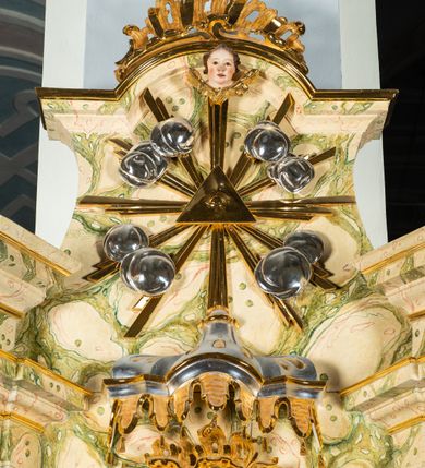 Zdjęcie nr 6: Ołtarz architektoniczny, jednoosiowy, jednokondygnacyjny, ze zwieńczeniem. Ołtarz prostopadłościenny z drewnianą, współczesną mensą i współczesnym antependium z przedstawieniem świętej w otoczeniu wieńca z kwiatami. Nastawa ujęta ukośnie dostawionymi filarami kanelowanymi, ustawionymi na postumentach z konsolami o prostych kapitelach utworzonych z roccailli i konsol podtrzymujących przerwane belkowanie zwieńczone ćwierćkolistymi naczółkami. Zwieńczenie o wklęsłych bokach zakończone profilowanym gzymsem w kształcie łuku nadwieszonego półkolistego. Na tle filaru, na konsolach ustawione figury uskrzydlonych aniołów. W polu środkowym obraz w kształcie stojącego prostokąta zamkniętego łukiem nadwieszonym półkolistym ozdobiony rocaillem. W ramie obraz z przedstawieniem św. Anny Samotrzeciej z Madonną z Dzieciątkiem. Nad ramą baldachim z lambrekinem. W zwieńczeniu serce Gorejące na tle glorii promienistej z chmurkami, zwieńczonej uskrzydloną główką anielską; nad gzymsem zwieńczenia  grzebień utworzony z ażurowego rocaillu. 