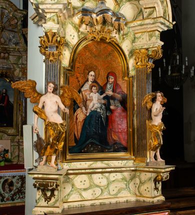 Zdjęcie nr 1: Ołtarz architektoniczny, jednoosiowy, jednokondygnacyjny, ze zwieńczeniem. Ołtarz prostopadłościenny z drewnianą, współczesną mensą i współczesnym antependium z przedstawieniem świętej w otoczeniu wieńca z kwiatami. Nastawa ujęta ukośnie dostawionymi filarami kanelowanymi, ustawionymi na postumentach z konsolami o prostych kapitelach utworzonych z roccailli i konsol podtrzymujących przerwane belkowanie zwieńczone ćwierćkolistymi naczółkami. Zwieńczenie o wklęsłych bokach zakończone profilowanym gzymsem w kształcie łuku nadwieszonego półkolistego. Na tle filaru, na konsolach ustawione figury uskrzydlonych aniołów. W polu środkowym obraz w kształcie stojącego prostokąta zamkniętego łukiem nadwieszonym półkolistym ozdobiony rocaillem. W ramie obraz z przedstawieniem św. Anny Samotrzeciej z Madonną z Dzieciątkiem. Nad ramą baldachim z lambrekinem. W zwieńczeniu serce Gorejące na tle glorii promienistej z chmurkami, zwieńczonej uskrzydloną główką anielską; nad gzymsem zwieńczenia  grzebień utworzony z ażurowego rocaillu. 