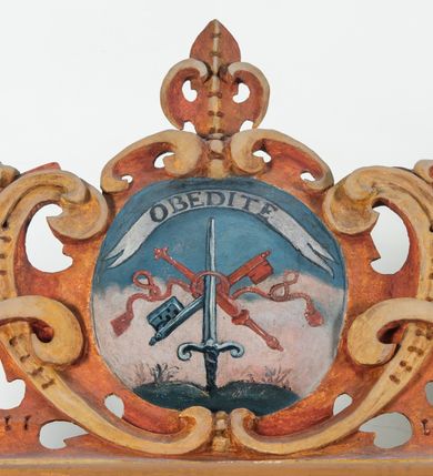 Zdjęcie nr 56: Umeblowanie zakrystii usytuowane jest wzdłuż ścian północnej, południowej i wschodniej pomieszczenia.  Na ścianie północnej, w części dolnej znajdują się trzy połączone ze sobą komody, każda o czterech szufladach, nakryte jednym blatem. W części górnej mieszczą się pięcioosiowe szafki z szufladami w cokole. Osie artykułowe są pilastrami hermowymi. Na osi środkowej szafka jest nieco wyższa i szersza z drzwiczkami dekorowanymi prostokątną, uszatą, oprofilowaną płyciną z malowanym przedstawieniem Chrystusa Eucharystycznego. Drzwiczki pozostałych szafek mają kształt stojących prostokątów i dekorowane są płycinami o wklęsłych narożach, zdobionymi gałązkami czerwonych róż, ułożonych w rokokowych wazonach. Ścianki zamknięte są niepełnym belkowaniem z gzymsem. W partii zwieńczenia osie artykułowane są cokolikami, na których ustawione są toczone, kuliste wazoniki. Pomiędzy nimi umieszczone są kartusze utworzone z ornamentu małżowinowo-chrząstkowego z malowanymi emblematami na owalnych medalionach, które ułożone są kolejno od lewej strony: 
1. Pionowo ustawiony miecz, ostrzem skierowany ku górze, połączony ze skrzyżowanymi berłem i dwoma kluczami, od których odchodzą fantazyjnie ułożone sznury w kolorze czerwonym. U góry napis na szarfie: „OBEDITE”.
2. W górnej części wyłaniająca się z chmur ręka trzymająca w dłoni węgielnicę i przymocowane do niej na łańcuszku tablice Dekalogu. Napis na szarfie: „OMNIA SVSTINET”.
3. Bóg Ojciec ukazany w półpostaci, lewą ręką opiera się na kuli ziemskiej, prawą czyni gest błogosławieństwa. 
4. Bujnie ulistnione, ciemnozielone drzewko spięte w dolnej części złotą formą w kształcie dwóch wywiniętych wolutek. Napis na szarfie: „GAVDET PATIENTIA DVRIS”. 
5. W górnej części obrazu z chmur wyłania się ręka, która zrzuca na ziemię iskrzący pocisk i dwa skrzyżowane pioruny, połączone parą białych skrzydeł. Napis „FORTIS VLTOR”.
 
Na ścianie środkowej, wschodniej znajduje się sarkofagowa mensa, powyżej parawanowa ścianka na profilowanym cokole, artykułowana pilastrami, pomiędzy którymi umieszczone są płyciny z kształcie leżących prostokątów z obrazami; ścianka zamknięta jest profilowanym gzymsem. W zwieńczeniu, na jej skrajach znajdują się owalne medaliony ujęte w kartusze z ornamentu małżowinowo-chrząstkowego. W medalionie po lewej stronie namalowane są litery alfa i omega na błękitnym tle oraz wstęga z napisem: „RENOVATUM A(NNO) D(OMINI) 1975”. Po prawej stronie analogiczny kartusz z literami w medalionie: „Ω / O / N” wpisane w formę krzyża, otoczonego niepełną aureolą; powyżej wstęga z napisem: „VIDENTEM AUDERE”. W płycinach obrazy przedstawiają świętych w ujęciu do pasa, zwróconych ku środkowi; od lewej:
1. Święty Demetriusz z włócznią opartą o prawy bark, ubrany w habit zakonu kanoników laterańskich od pokuty.
2. Święty Klet z aniołkiem, który trzyma w dłoni palmę męczeństwa i krzyż papieski. W prawym górnym narożu obrazu napis: „FAC HVIC SIGNO HONOREM”.
3. Święty Augustyn z gorejącym sercem na piersi i aniołkiem z łyżką i miseczką w dłoniach.
4. Święty ubrany w habit Marków, który trzyma w dłoni serce z krzyżem, podtrzymywane przez Chrystusa na obłokach – prawdopodobnie św. Cyriak, założyciel zakonu.
 
Na ścianie południowej znajduje się analogiczne umeblowanie, jak na ścianie północnej. W dolnej części dwie komody, a w miejscu trzeciej od wschodu szafka zdobiona dwiema uszatymi płycinami. Górna część mebla w przeciwieństwie do ściany północnej bez podwyższenia części środkowej. 
Na ścianie południowej:
1. Jasnobrązowa harfa na błękitnym tle i napis: „IN DOMINO”.
2. Ciemnobrązowy ptak i trzy podrywające się do lotu młode, w górnej części złote słońce i napis: „NON QUAE SVPER TERRAM.”
3. Po lewej stronie kompozycji wyłaniająca się z chmur ręka trzymająca skrzyżowane: miecz, czerwony krzyż i palmę. Napis: „NON ERVBESCO”.
4. W centrum przedstawienia krzak białej lilii o trzech rozgałęzieniach, w tle chmury w odcieniach koloru szaroniebieskiego. Napis na szarfie: „PER ARDVA DVLCIS”.
5. W lewej części kompozycji uskrzydlony jeleń, wspięty na tylnych nogach, po prawej stronie czarne i brązowe skały, w partii górnej otwarta korona, umieszczona pośrodku obłoku obwiedzionego biało-czerwonym pasem. Napis: „ET COMPREHENDATIS”.
 
W miejscu połączenia komód ścian północnej i południowej z dolną częścią konstrukcji na ścianie wschodniej znajdują się ukośnie ustawione, jednoskrzydłowe szafki o drzwiczkach dekorowanych prostokątną płyciną o wklęsłych narożach. Ścianki boczne części północnej i południowej zdobione są ukośną kratką. Powierzchnia szafek i komód pokryta jest polichromią imitującą marmur w kolorze beżowym, szarokremowym, różowym i rdzawym. Blaty malowane są farbą olejną w kolorze beżowym. Obramienia medalionów malowane w kolorze rdzawozłotym. Tło w większości medalionów w odcieniach błękitu, w górnych częściach majuskułowe napisy objaśniające przedstawienie, umieszczone w białych i półkoliście ułożonych szarfach. 