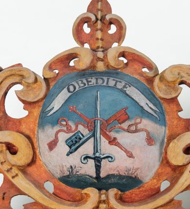 Zdjęcie nr 78: Umeblowanie zakrystii usytuowane jest wzdłuż ścian północnej, południowej i wschodniej pomieszczenia.  Na ścianie północnej, w części dolnej znajdują się trzy połączone ze sobą komody, każda o czterech szufladach, nakryte jednym blatem. W części górnej mieszczą się pięcioosiowe szafki z szufladami w cokole. Osie artykułowe są pilastrami hermowymi. Na osi środkowej szafka jest nieco wyższa i szersza z drzwiczkami dekorowanymi prostokątną, uszatą, oprofilowaną płyciną z malowanym przedstawieniem Chrystusa Eucharystycznego. Drzwiczki pozostałych szafek mają kształt stojących prostokątów i dekorowane są płycinami o wklęsłych narożach, zdobionymi gałązkami czerwonych róż, ułożonych w rokokowych wazonach. Ścianki zamknięte są niepełnym belkowaniem z gzymsem. W partii zwieńczenia osie artykułowane są cokolikami, na których ustawione są toczone, kuliste wazoniki. Pomiędzy nimi umieszczone są kartusze utworzone z ornamentu małżowinowo-chrząstkowego z malowanymi emblematami na owalnych medalionach, które ułożone są kolejno od lewej strony: 
1. Pionowo ustawiony miecz, ostrzem skierowany ku górze, połączony ze skrzyżowanymi berłem i dwoma kluczami, od których odchodzą fantazyjnie ułożone sznury w kolorze czerwonym. U góry napis na szarfie: „OBEDITE”.
2. W górnej części wyłaniająca się z chmur ręka trzymająca w dłoni węgielnicę i przymocowane do niej na łańcuszku tablice Dekalogu. Napis na szarfie: „OMNIA SVSTINET”.
3. Bóg Ojciec ukazany w półpostaci, lewą ręką opiera się na kuli ziemskiej, prawą czyni gest błogosławieństwa. 
4. Bujnie ulistnione, ciemnozielone drzewko spięte w dolnej części złotą formą w kształcie dwóch wywiniętych wolutek. Napis na szarfie: „GAVDET PATIENTIA DVRIS”. 
5. W górnej części obrazu z chmur wyłania się ręka, która zrzuca na ziemię iskrzący pocisk i dwa skrzyżowane pioruny, połączone parą białych skrzydeł. Napis „FORTIS VLTOR”.
 
Na ścianie środkowej, wschodniej znajduje się sarkofagowa mensa, powyżej parawanowa ścianka na profilowanym cokole, artykułowana pilastrami, pomiędzy którymi umieszczone są płyciny z kształcie leżących prostokątów z obrazami; ścianka zamknięta jest profilowanym gzymsem. W zwieńczeniu, na jej skrajach znajdują się owalne medaliony ujęte w kartusze z ornamentu małżowinowo-chrząstkowego. W medalionie po lewej stronie namalowane są litery alfa i omega na błękitnym tle oraz wstęga z napisem: „RENOVATUM A(NNO) D(OMINI) 1975”. Po prawej stronie analogiczny kartusz z literami w medalionie: „Ω / O / N” wpisane w formę krzyża, otoczonego niepełną aureolą; powyżej wstęga z napisem: „VIDENTEM AUDERE”. W płycinach obrazy przedstawiają świętych w ujęciu do pasa, zwróconych ku środkowi; od lewej:
1. Święty Demetriusz z włócznią opartą o prawy bark, ubrany w habit zakonu kanoników laterańskich od pokuty.
2. Święty Klet z aniołkiem, który trzyma w dłoni palmę męczeństwa i krzyż papieski. W prawym górnym narożu obrazu napis: „FAC HVIC SIGNO HONOREM”.
3. Święty Augustyn z gorejącym sercem na piersi i aniołkiem z łyżką i miseczką w dłoniach.
4. Święty ubrany w habit Marków, który trzyma w dłoni serce z krzyżem, podtrzymywane przez Chrystusa na obłokach – prawdopodobnie św. Cyriak, założyciel zakonu.
 
Na ścianie południowej znajduje się analogiczne umeblowanie, jak na ścianie północnej. W dolnej części dwie komody, a w miejscu trzeciej od wschodu szafka zdobiona dwiema uszatymi płycinami. Górna część mebla w przeciwieństwie do ściany północnej bez podwyższenia części środkowej. 
Na ścianie południowej:
1. Jasnobrązowa harfa na błękitnym tle i napis: „IN DOMINO”.
2. Ciemnobrązowy ptak i trzy podrywające się do lotu młode, w górnej części złote słońce i napis: „NON QUAE SVPER TERRAM.”
3. Po lewej stronie kompozycji wyłaniająca się z chmur ręka trzymająca skrzyżowane: miecz, czerwony krzyż i palmę. Napis: „NON ERVBESCO”.
4. W centrum przedstawienia krzak białej lilii o trzech rozgałęzieniach, w tle chmury w odcieniach koloru szaroniebieskiego. Napis na szarfie: „PER ARDVA DVLCIS”.
5. W lewej części kompozycji uskrzydlony jeleń, wspięty na tylnych nogach, po prawej stronie czarne i brązowe skały, w partii górnej otwarta korona, umieszczona pośrodku obłoku obwiedzionego biało-czerwonym pasem. Napis: „ET COMPREHENDATIS”.
 
W miejscu połączenia komód ścian północnej i południowej z dolną częścią konstrukcji na ścianie wschodniej znajdują się ukośnie ustawione, jednoskrzydłowe szafki o drzwiczkach dekorowanych prostokątną płyciną o wklęsłych narożach. Ścianki boczne części północnej i południowej zdobione są ukośną kratką. Powierzchnia szafek i komód pokryta jest polichromią imitującą marmur w kolorze beżowym, szarokremowym, różowym i rdzawym. Blaty malowane są farbą olejną w kolorze beżowym. Obramienia medalionów malowane w kolorze rdzawozłotym. Tło w większości medalionów w odcieniach błękitu, w górnych częściach majuskułowe napisy objaśniające przedstawienie, umieszczone w białych i półkoliście ułożonych szarfach. 