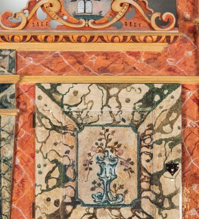 Zdjęcie nr 67: Umeblowanie zakrystii usytuowane jest wzdłuż ścian północnej, południowej i wschodniej pomieszczenia.  Na ścianie północnej, w części dolnej znajdują się trzy połączone ze sobą komody, każda o czterech szufladach, nakryte jednym blatem. W części górnej mieszczą się pięcioosiowe szafki z szufladami w cokole. Osie artykułowe są pilastrami hermowymi. Na osi środkowej szafka jest nieco wyższa i szersza z drzwiczkami dekorowanymi prostokątną, uszatą, oprofilowaną płyciną z malowanym przedstawieniem Chrystusa Eucharystycznego. Drzwiczki pozostałych szafek mają kształt stojących prostokątów i dekorowane są płycinami o wklęsłych narożach, zdobionymi gałązkami czerwonych róż, ułożonych w rokokowych wazonach. Ścianki zamknięte są niepełnym belkowaniem z gzymsem. W partii zwieńczenia osie artykułowane są cokolikami, na których ustawione są toczone, kuliste wazoniki. Pomiędzy nimi umieszczone są kartusze utworzone z ornamentu małżowinowo-chrząstkowego z malowanymi emblematami na owalnych medalionach, które ułożone są kolejno od lewej strony: 
1. Pionowo ustawiony miecz, ostrzem skierowany ku górze, połączony ze skrzyżowanymi berłem i dwoma kluczami, od których odchodzą fantazyjnie ułożone sznury w kolorze czerwonym. U góry napis na szarfie: „OBEDITE”.
2. W górnej części wyłaniająca się z chmur ręka trzymająca w dłoni węgielnicę i przymocowane do niej na łańcuszku tablice Dekalogu. Napis na szarfie: „OMNIA SVSTINET”.
3. Bóg Ojciec ukazany w półpostaci, lewą ręką opiera się na kuli ziemskiej, prawą czyni gest błogosławieństwa. 
4. Bujnie ulistnione, ciemnozielone drzewko spięte w dolnej części złotą formą w kształcie dwóch wywiniętych wolutek. Napis na szarfie: „GAVDET PATIENTIA DVRIS”. 
5. W górnej części obrazu z chmur wyłania się ręka, która zrzuca na ziemię iskrzący pocisk i dwa skrzyżowane pioruny, połączone parą białych skrzydeł. Napis „FORTIS VLTOR”.
 
Na ścianie środkowej, wschodniej znajduje się sarkofagowa mensa, powyżej parawanowa ścianka na profilowanym cokole, artykułowana pilastrami, pomiędzy którymi umieszczone są płyciny z kształcie leżących prostokątów z obrazami; ścianka zamknięta jest profilowanym gzymsem. W zwieńczeniu, na jej skrajach znajdują się owalne medaliony ujęte w kartusze z ornamentu małżowinowo-chrząstkowego. W medalionie po lewej stronie namalowane są litery alfa i omega na błękitnym tle oraz wstęga z napisem: „RENOVATUM A(NNO) D(OMINI) 1975”. Po prawej stronie analogiczny kartusz z literami w medalionie: „Ω / O / N” wpisane w formę krzyża, otoczonego niepełną aureolą; powyżej wstęga z napisem: „VIDENTEM AUDERE”. W płycinach obrazy przedstawiają świętych w ujęciu do pasa, zwróconych ku środkowi; od lewej:
1. Święty Demetriusz z włócznią opartą o prawy bark, ubrany w habit zakonu kanoników laterańskich od pokuty.
2. Święty Klet z aniołkiem, który trzyma w dłoni palmę męczeństwa i krzyż papieski. W prawym górnym narożu obrazu napis: „FAC HVIC SIGNO HONOREM”.
3. Święty Augustyn z gorejącym sercem na piersi i aniołkiem z łyżką i miseczką w dłoniach.
4. Święty ubrany w habit Marków, który trzyma w dłoni serce z krzyżem, podtrzymywane przez Chrystusa na obłokach – prawdopodobnie św. Cyriak, założyciel zakonu.
 
Na ścianie południowej znajduje się analogiczne umeblowanie, jak na ścianie północnej. W dolnej części dwie komody, a w miejscu trzeciej od wschodu szafka zdobiona dwiema uszatymi płycinami. Górna część mebla w przeciwieństwie do ściany północnej bez podwyższenia części środkowej. 
Na ścianie południowej:
1. Jasnobrązowa harfa na błękitnym tle i napis: „IN DOMINO”.
2. Ciemnobrązowy ptak i trzy podrywające się do lotu młode, w górnej części złote słońce i napis: „NON QUAE SVPER TERRAM.”
3. Po lewej stronie kompozycji wyłaniająca się z chmur ręka trzymająca skrzyżowane: miecz, czerwony krzyż i palmę. Napis: „NON ERVBESCO”.
4. W centrum przedstawienia krzak białej lilii o trzech rozgałęzieniach, w tle chmury w odcieniach koloru szaroniebieskiego. Napis na szarfie: „PER ARDVA DVLCIS”.
5. W lewej części kompozycji uskrzydlony jeleń, wspięty na tylnych nogach, po prawej stronie czarne i brązowe skały, w partii górnej otwarta korona, umieszczona pośrodku obłoku obwiedzionego biało-czerwonym pasem. Napis: „ET COMPREHENDATIS”.
 
W miejscu połączenia komód ścian północnej i południowej z dolną częścią konstrukcji na ścianie wschodniej znajdują się ukośnie ustawione, jednoskrzydłowe szafki o drzwiczkach dekorowanych prostokątną płyciną o wklęsłych narożach. Ścianki boczne części północnej i południowej zdobione są ukośną kratką. Powierzchnia szafek i komód pokryta jest polichromią imitującą marmur w kolorze beżowym, szarokremowym, różowym i rdzawym. Blaty malowane są farbą olejną w kolorze beżowym. Obramienia medalionów malowane w kolorze rdzawozłotym. Tło w większości medalionów w odcieniach błękitu, w górnych częściach majuskułowe napisy objaśniające przedstawienie, umieszczone w białych i półkoliście ułożonych szarfach. 